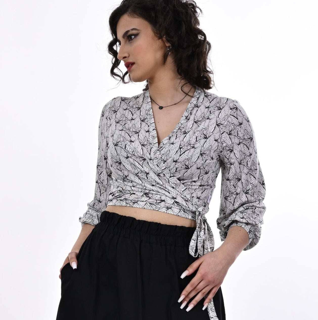 A model wearing a white and black wrap top with blouson sleeves and a wings print, paired with a long black skirt.