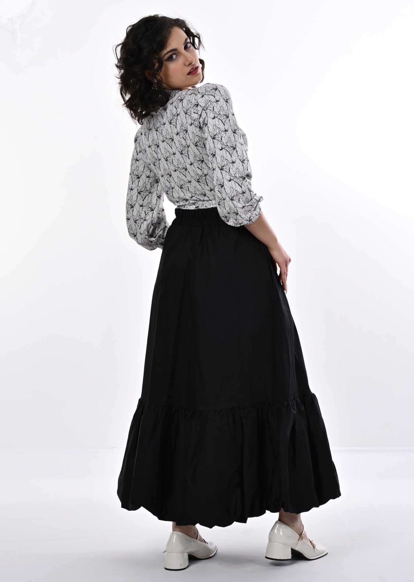 A model wearing a white and black wrap top with blouson sleeves and a wings print, paired with a long black skirt.