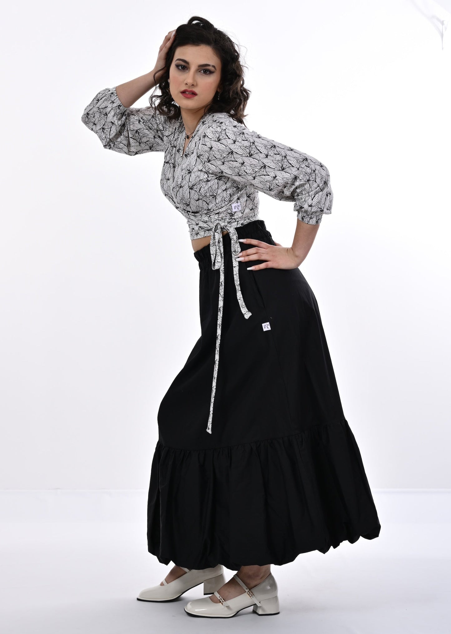 A model wearing a white and black wrap top with blouson sleeves and a wings print, paired with a long black skirt.