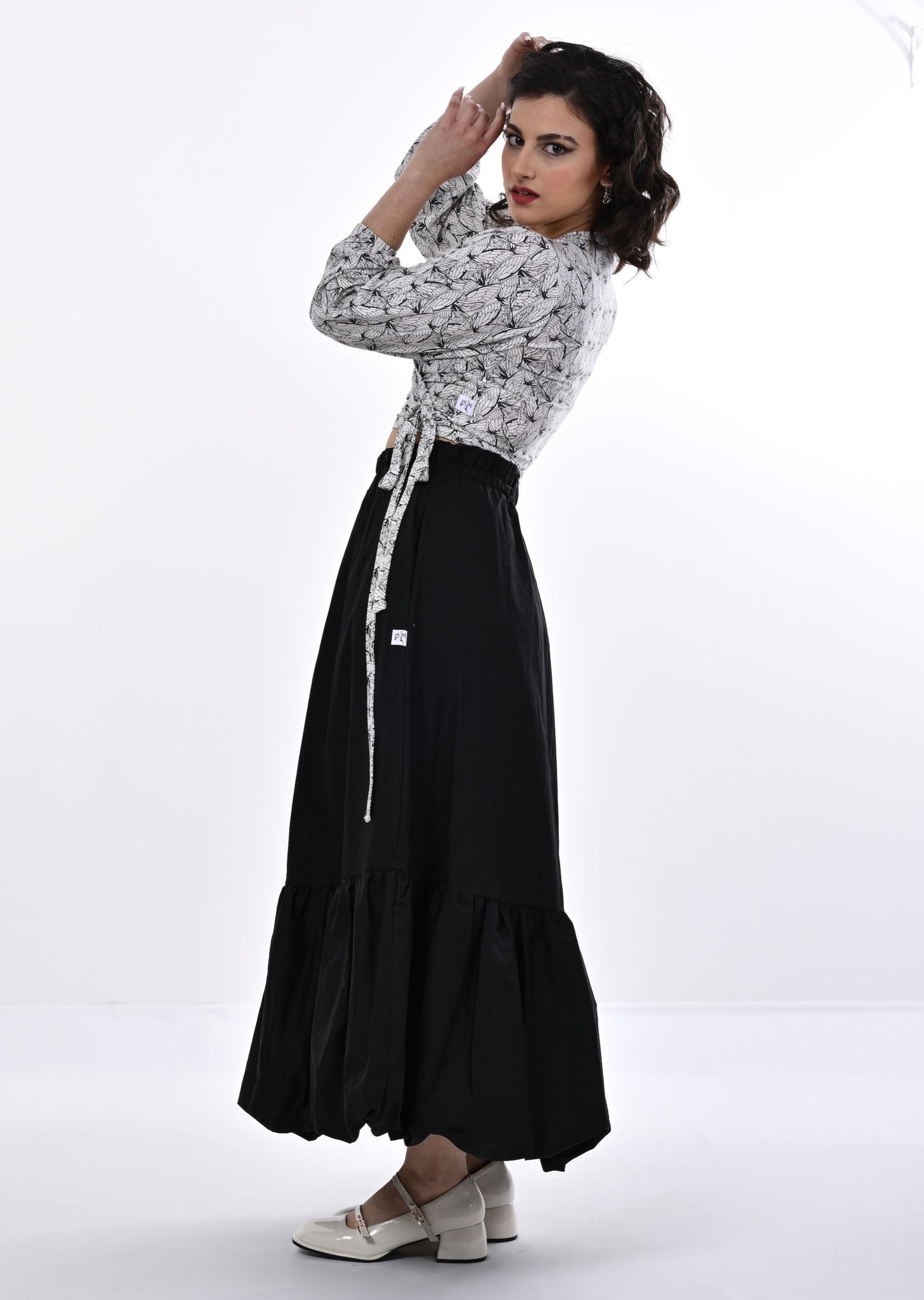 A model wearing a white and black wrap top with blouson sleeves and a wings print, paired with a long black skirt.