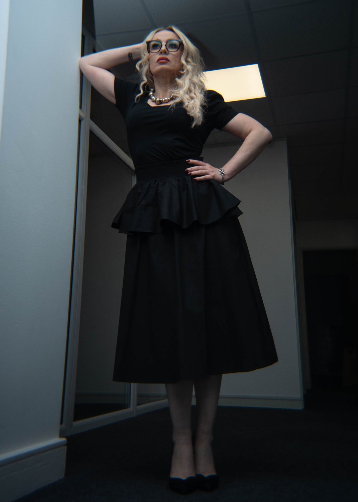 Woman in a black dress standing in a room with a light fixture.