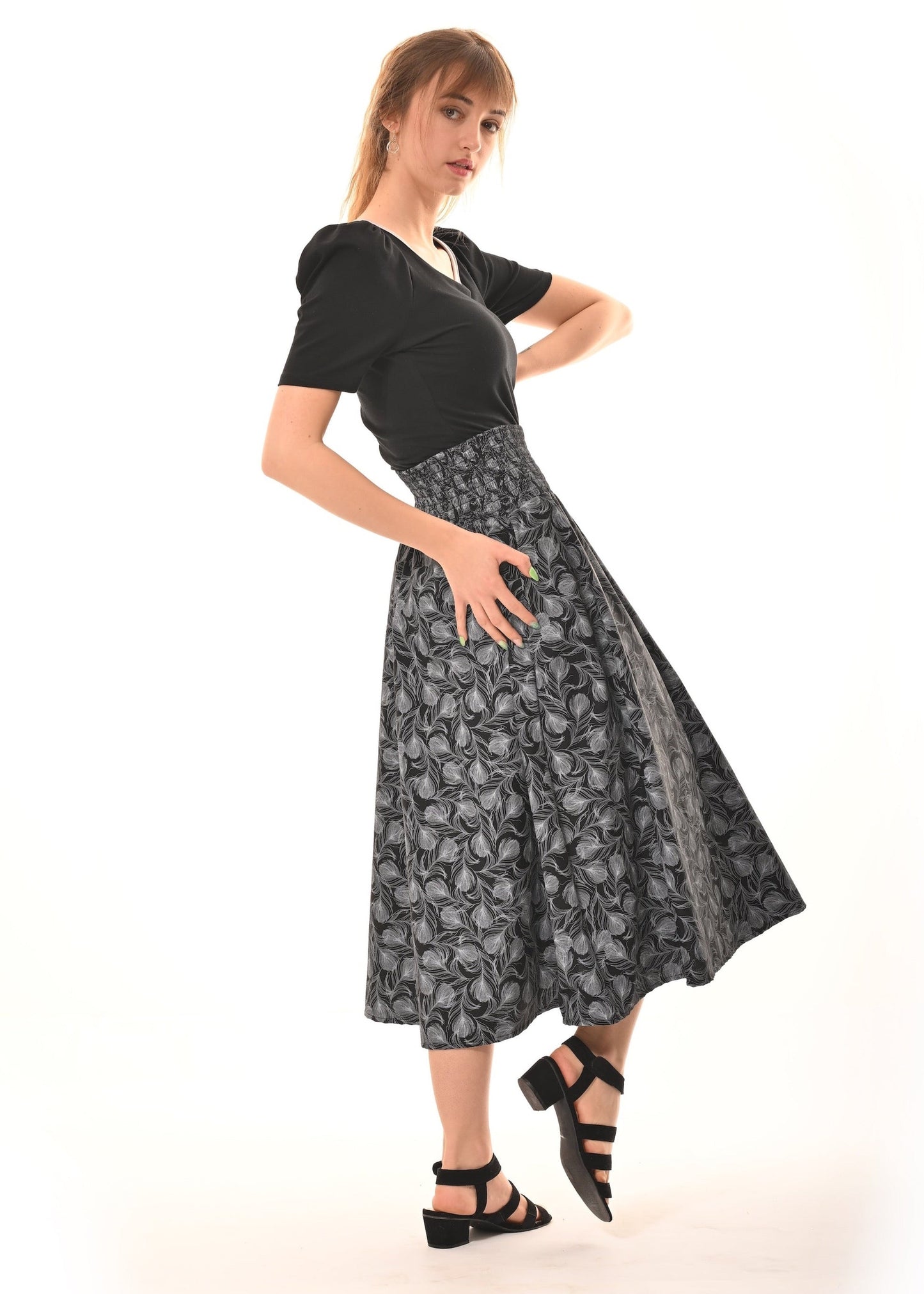 A woman modeling a black short-sleeve top paired with a high-waisted, flared midi skirt featuring a gray and black abstract floral pattern, styled with black strappy heels against a white studio background.