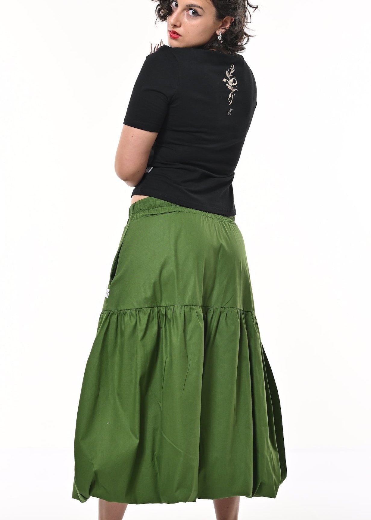 A woman modelling a green tiered puffball midi skirt with a gathered waist, paired with a black short-sleeve top and black heels.