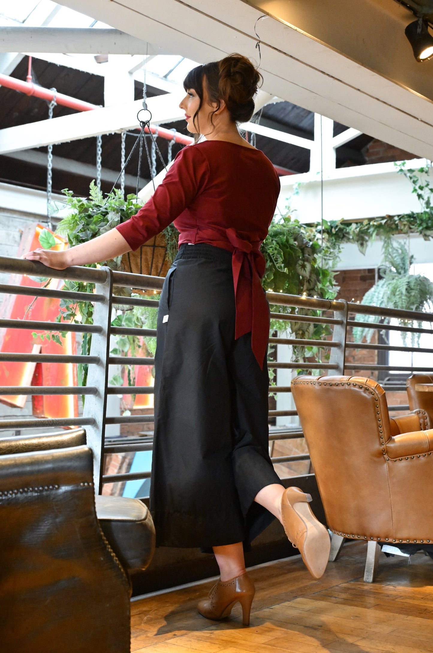 Woman standing in a modern indoor setting with plants and furniture.