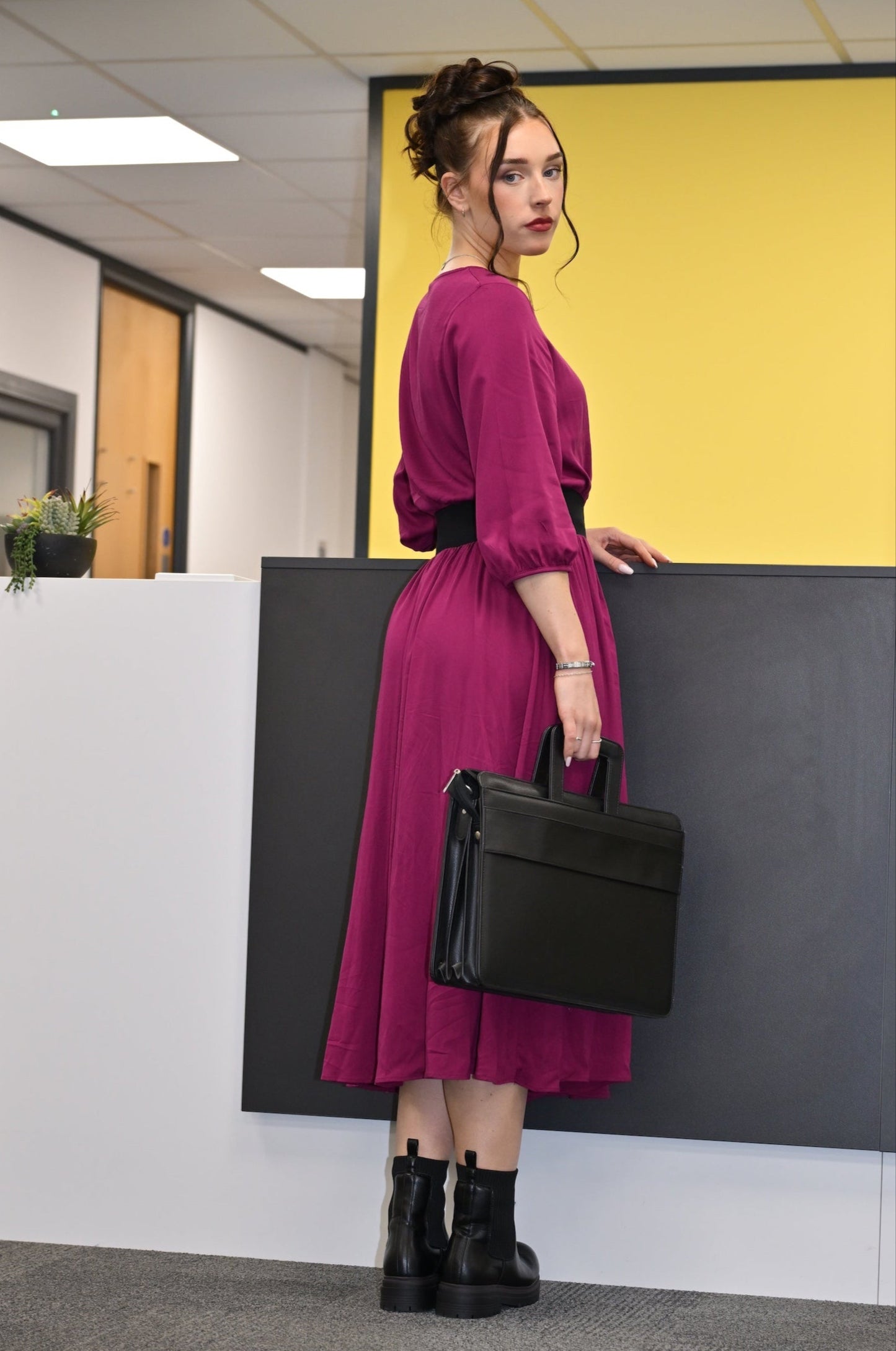 Woman in a magenta dress holding a black briefcase in an office setting