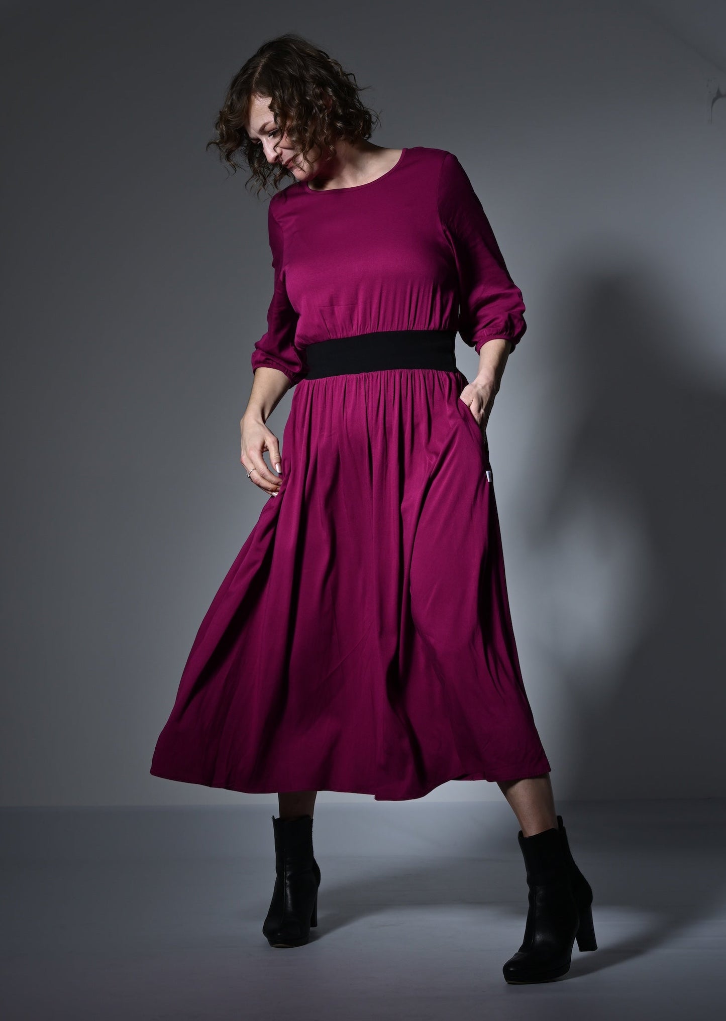 Woman wearing a magenta dress with a black belt against a gray background