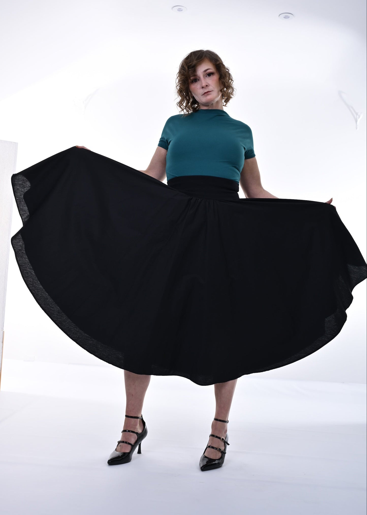 Woman wearing a teal top and black skirt in a studio setting