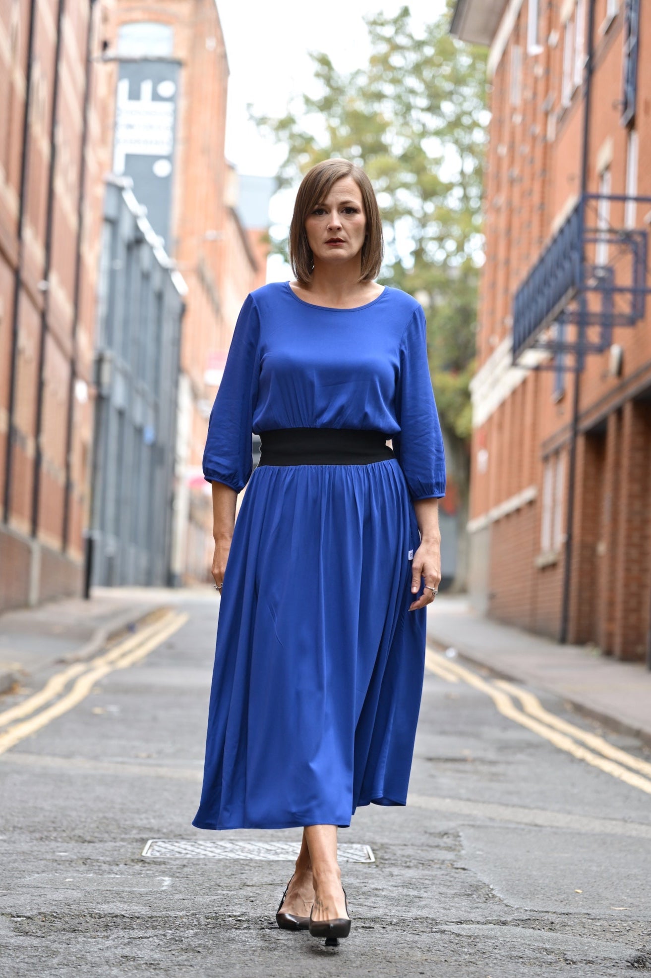 Woman wearing a blue outfit standing on a street with buildings in the background
