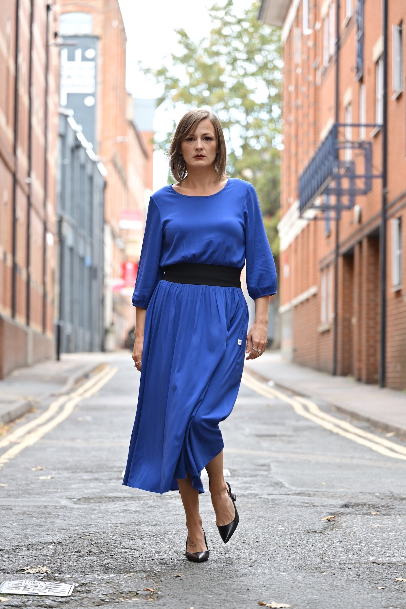 Woman in a blue dress walking down a street with brick buildings.