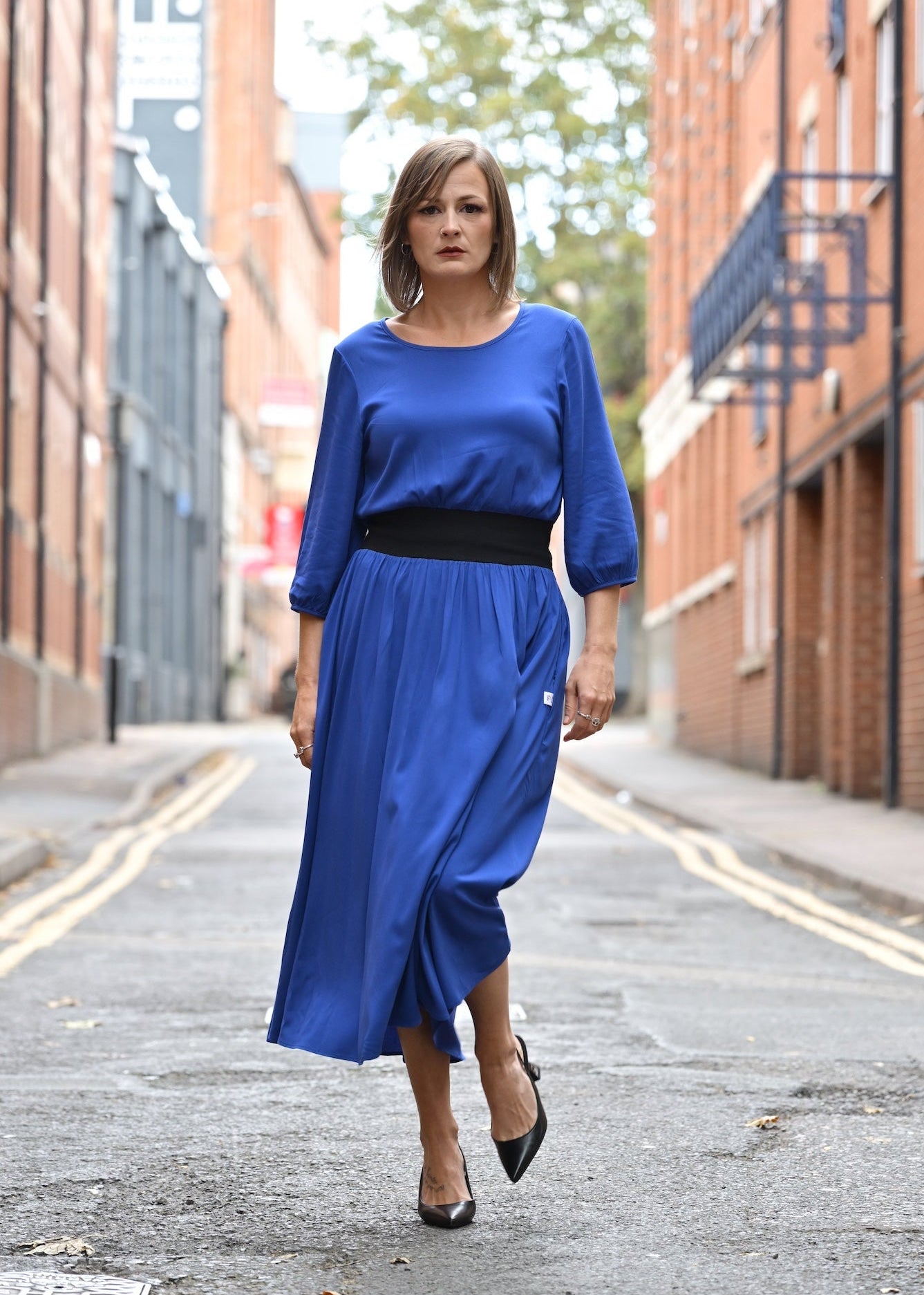 Woman in a blue dress walking down a street with brick buildings.