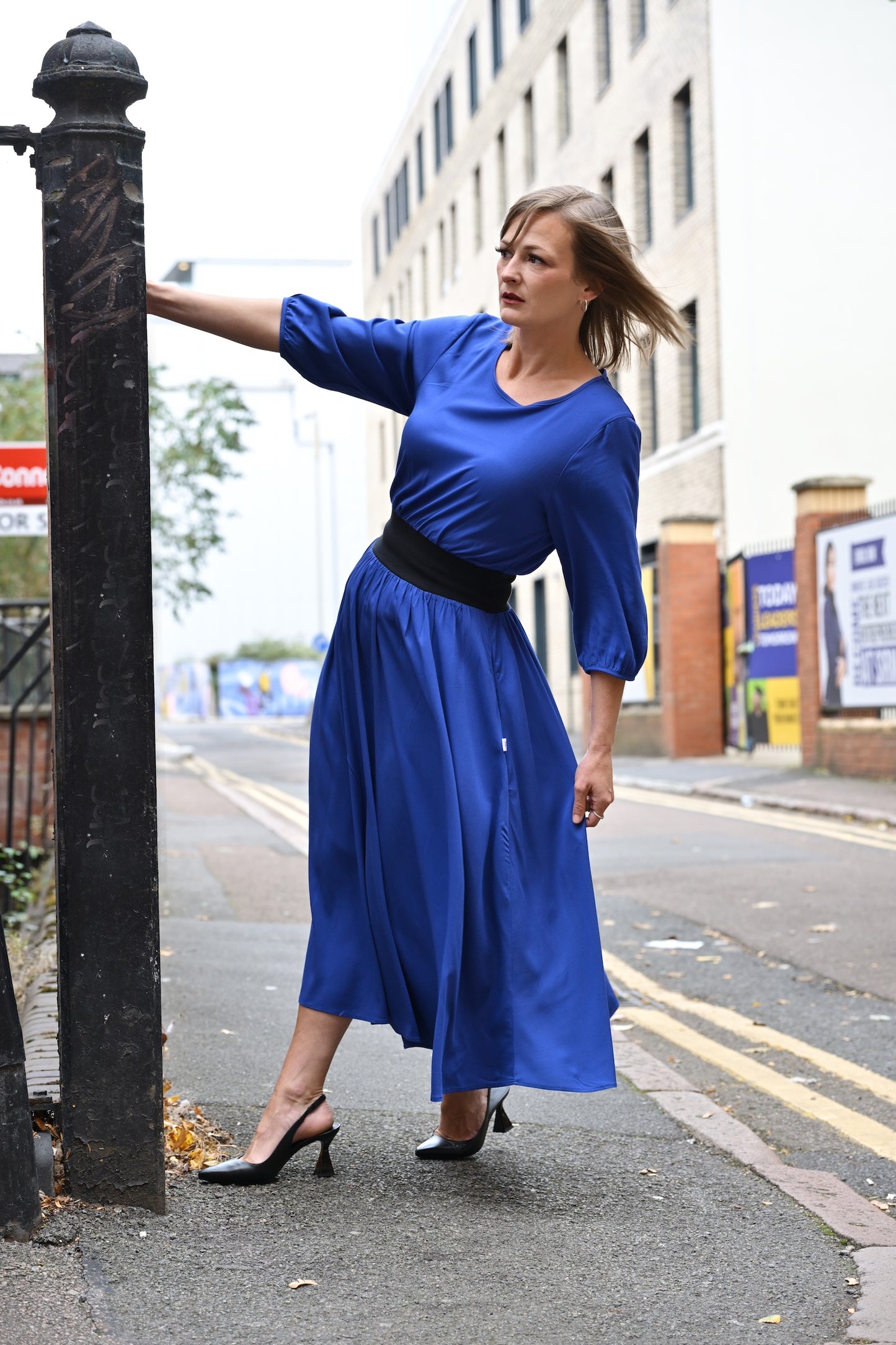 Woman in a blue dress standing on a street next to a black post.