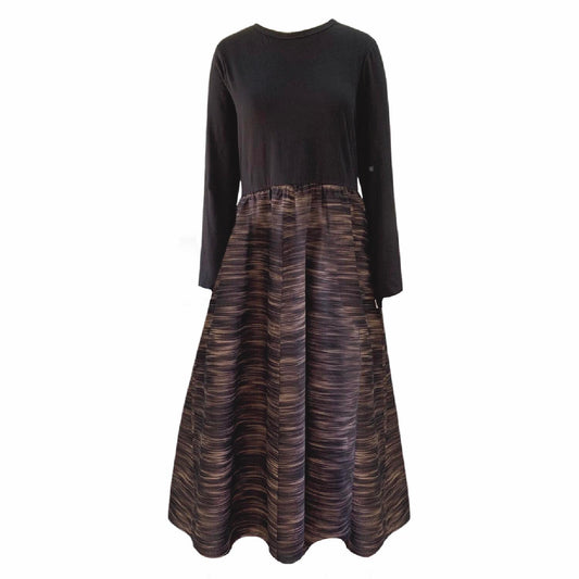 This is a midaxi style dress in dark silhouetted against a white background facing the front. The neckline is round and the sleeves are long. The top gathers in to the waist elastic and the skirt is full with side pockets. The dress is a midaxi length.