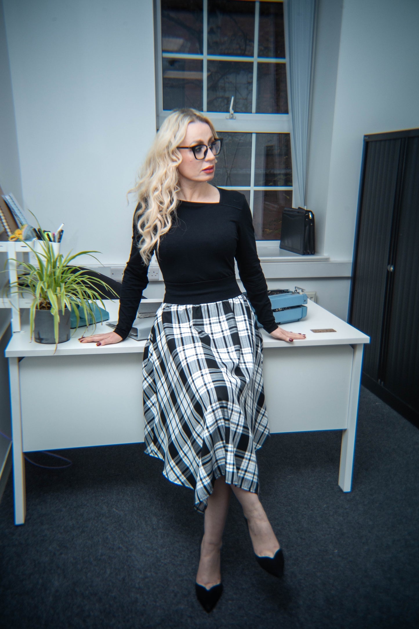 Woman in a black top and plaid skirt standing in an office setting.