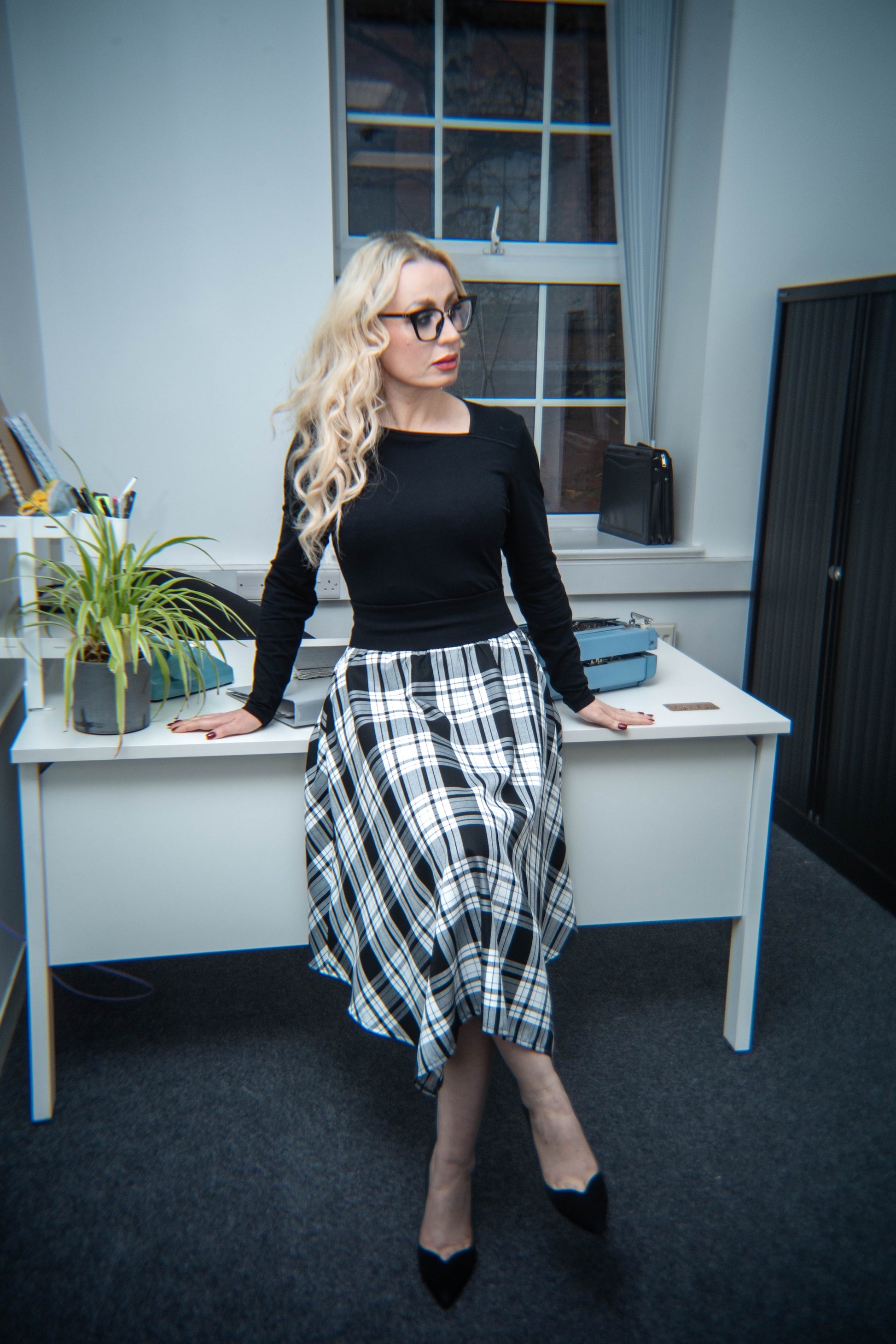 Woman in a black top and plaid skirt standing in an office setting.