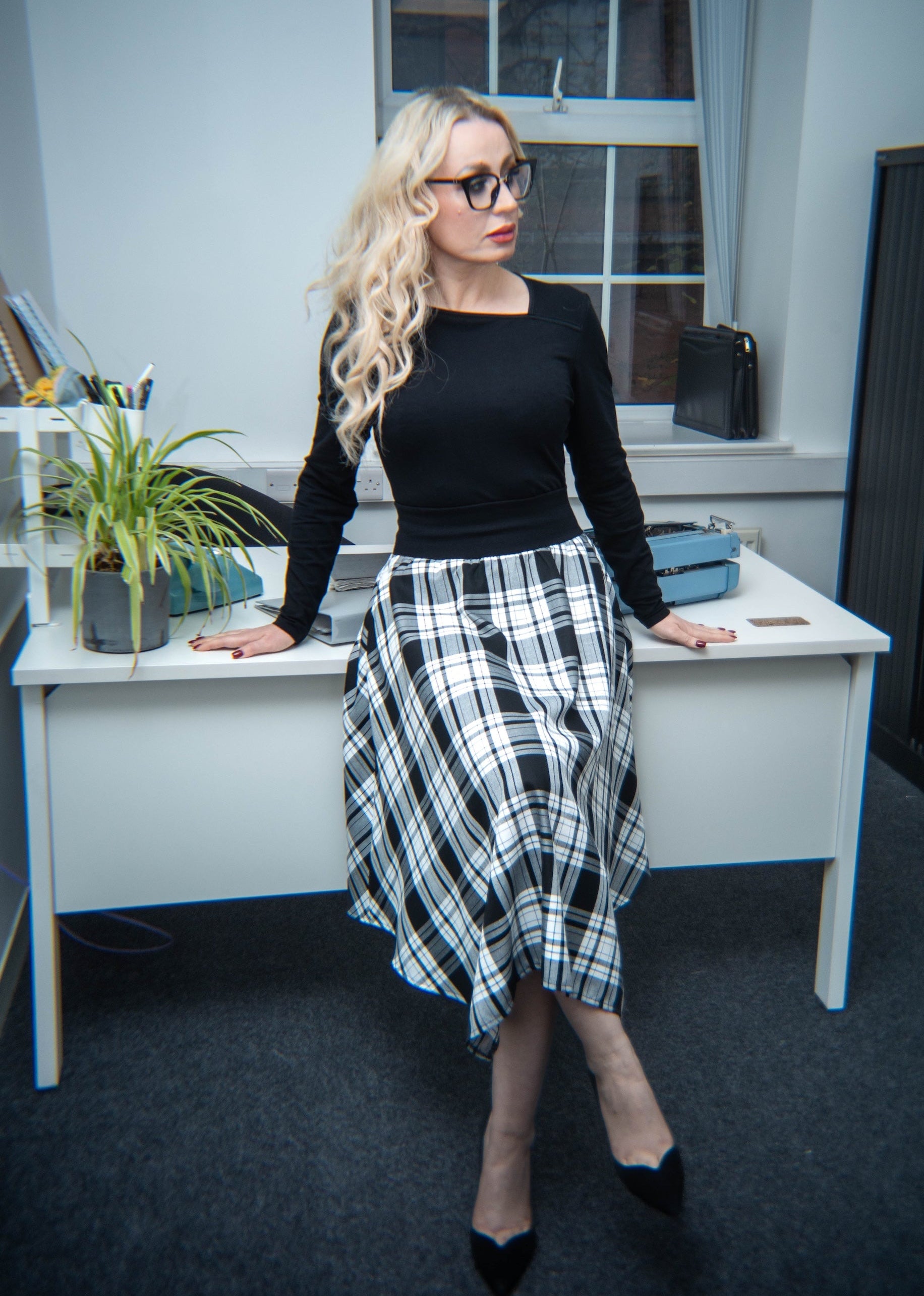 Woman in a black top and plaid skirt standing in an office setting.