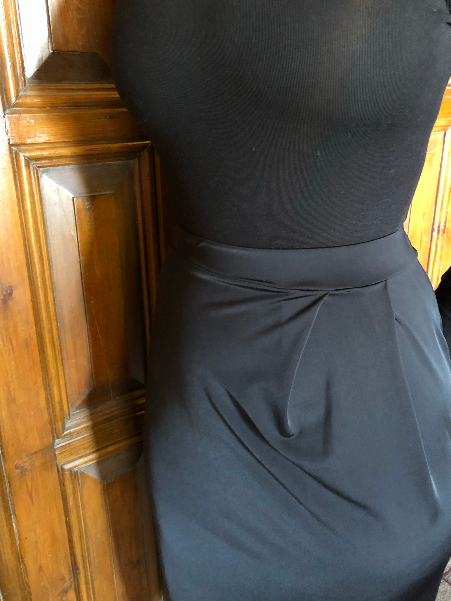 This is a close up of a black pencil style skirt, it has a waistband and pleated detail going into the waist.