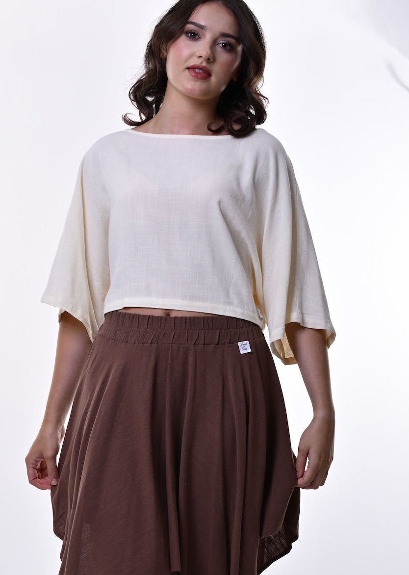 A woman modelling a cream-coloured crop top and a brown draped midi skirt against a bright white studio background.