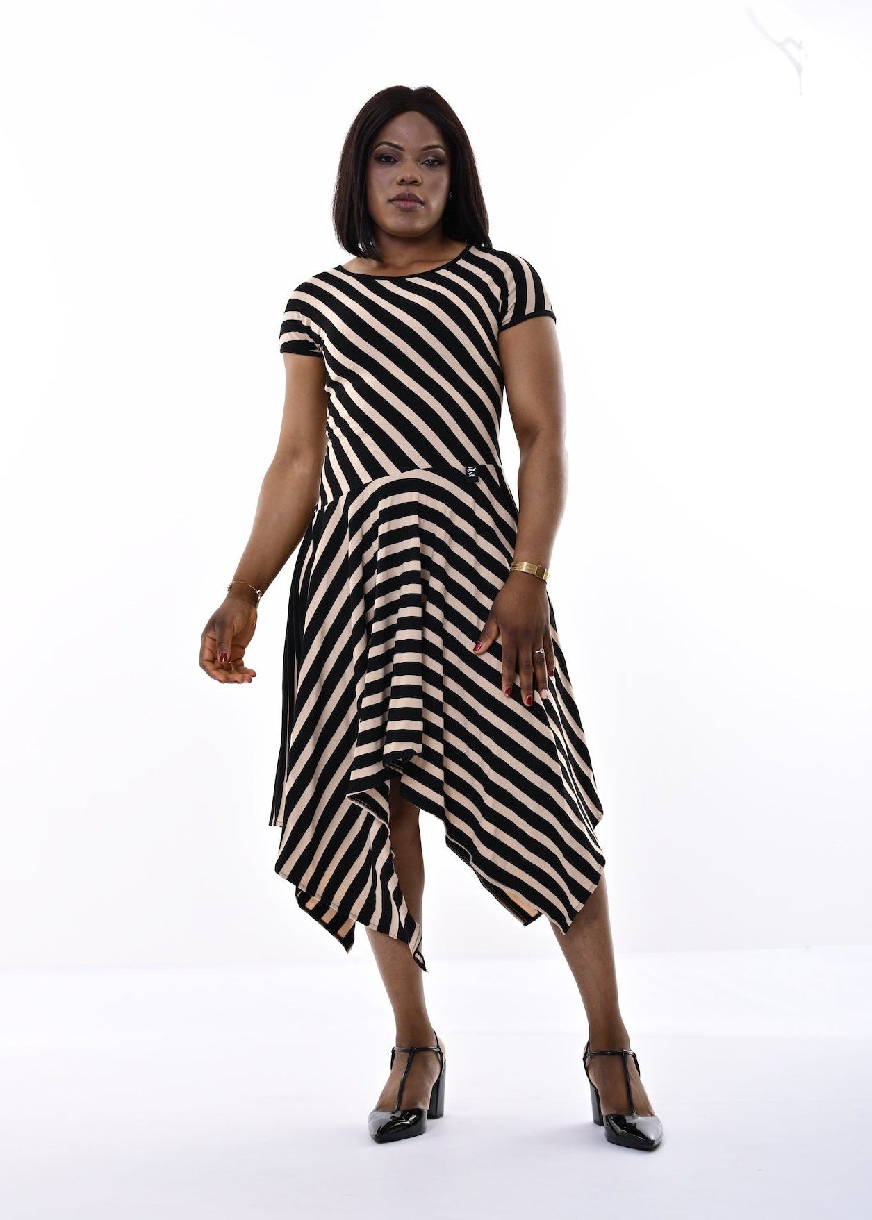 A woman modeling a short-sleeve midi dress with bold black and sand diagonal stripes, standing against a seamless white studio background.