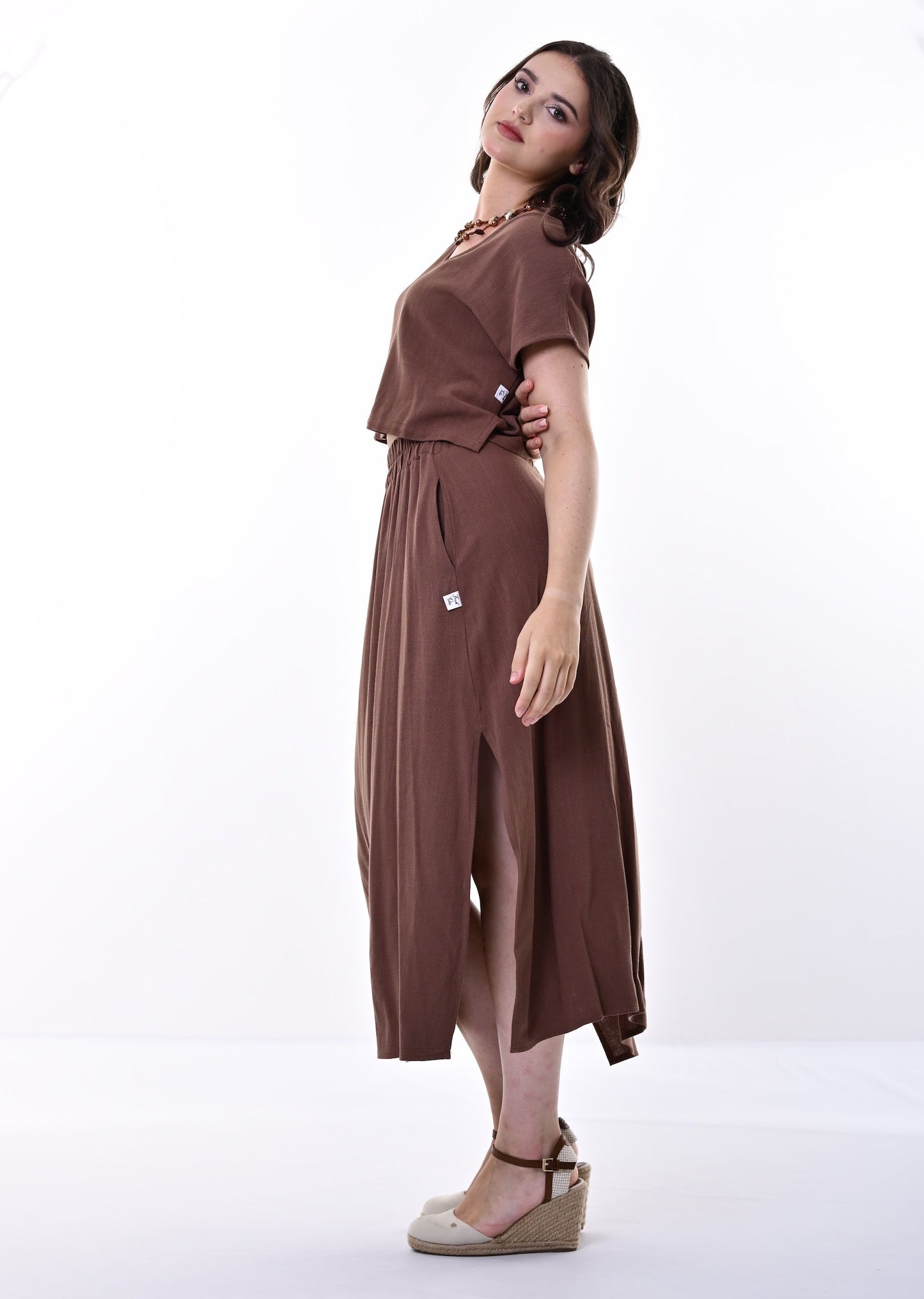 A woman modelling a brown top and skirt with a short-sleeve top and gathered skirt, standing in a white studio setting.