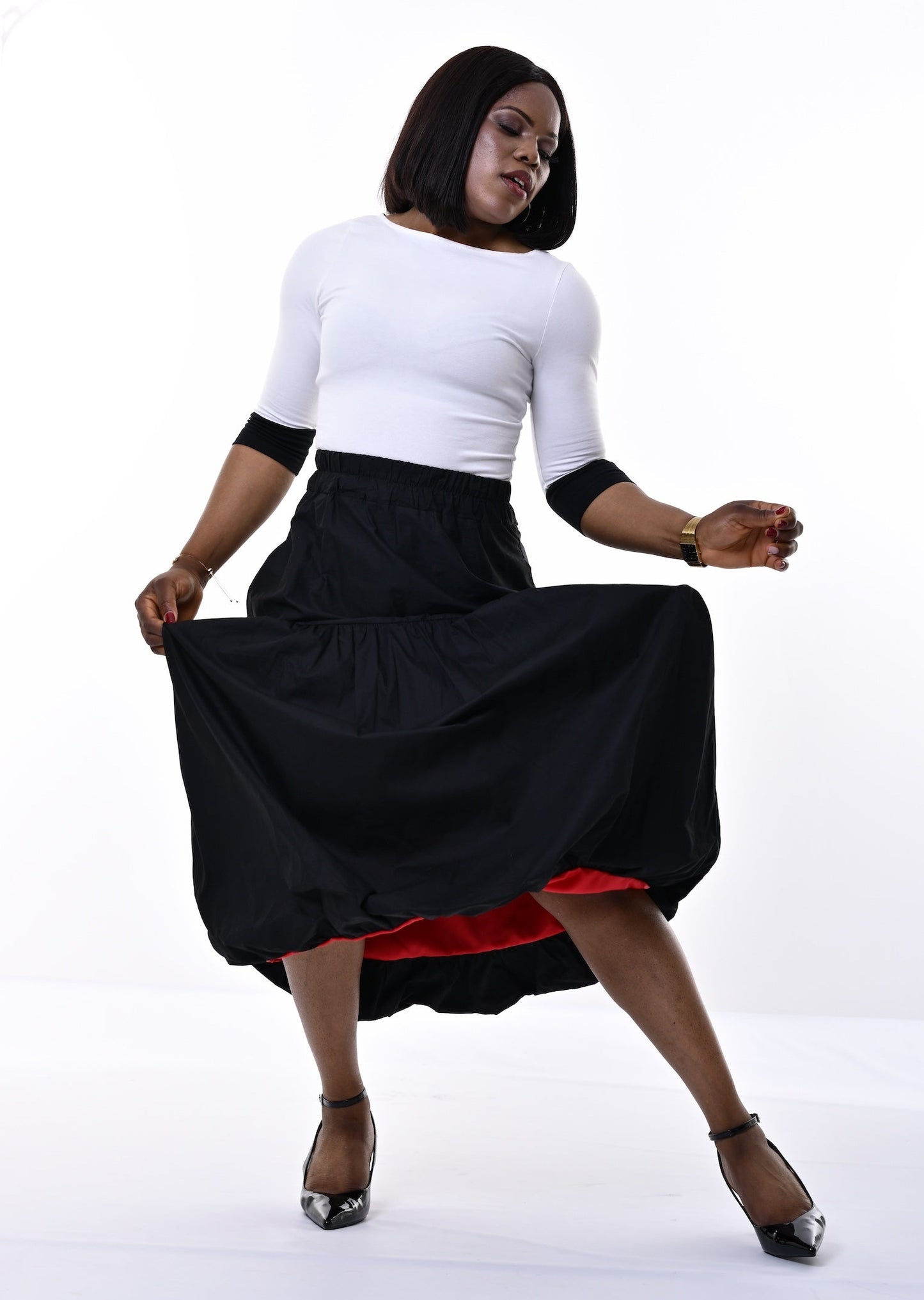 A woman posing in a white three-quarter sleeve top and a black skirt that reveals a red lining, set against a bright white studio background.