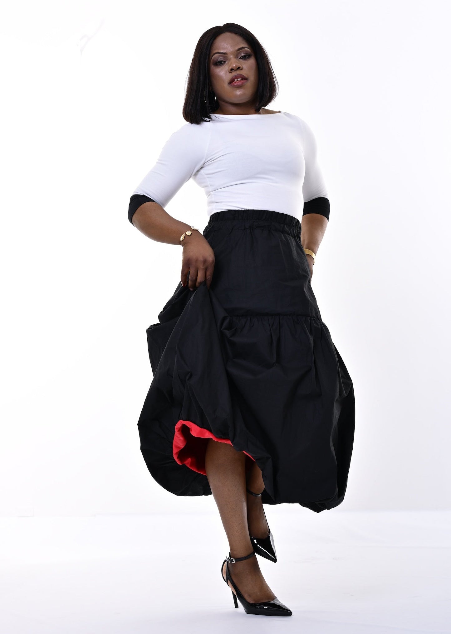 A woman modeling a black tiered maxi skirt with a red lining and a white top, standing against a bright white studio background.