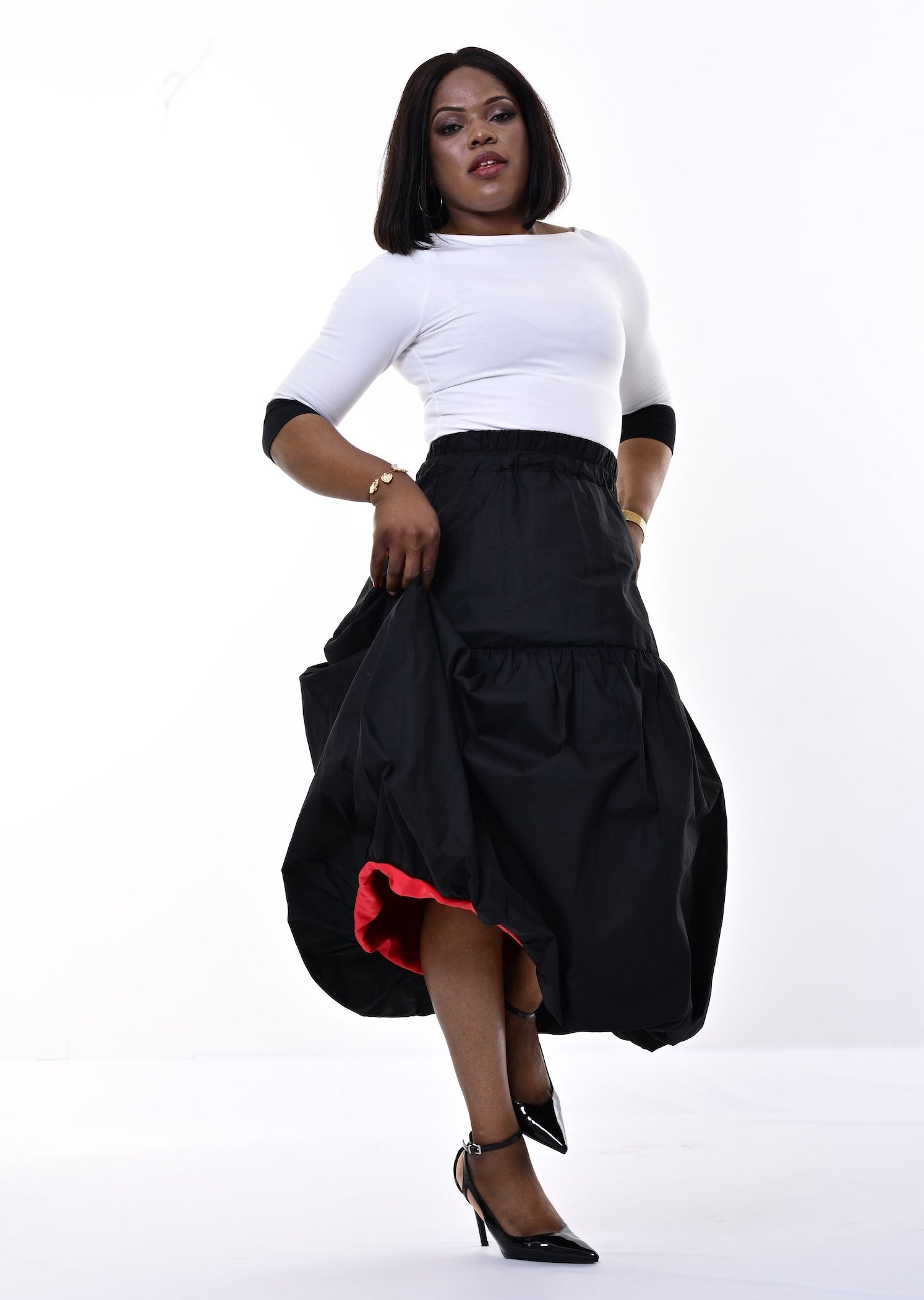 A woman modeling a black tiered maxi skirt with a red lining and a white top, standing against a bright white studio background.