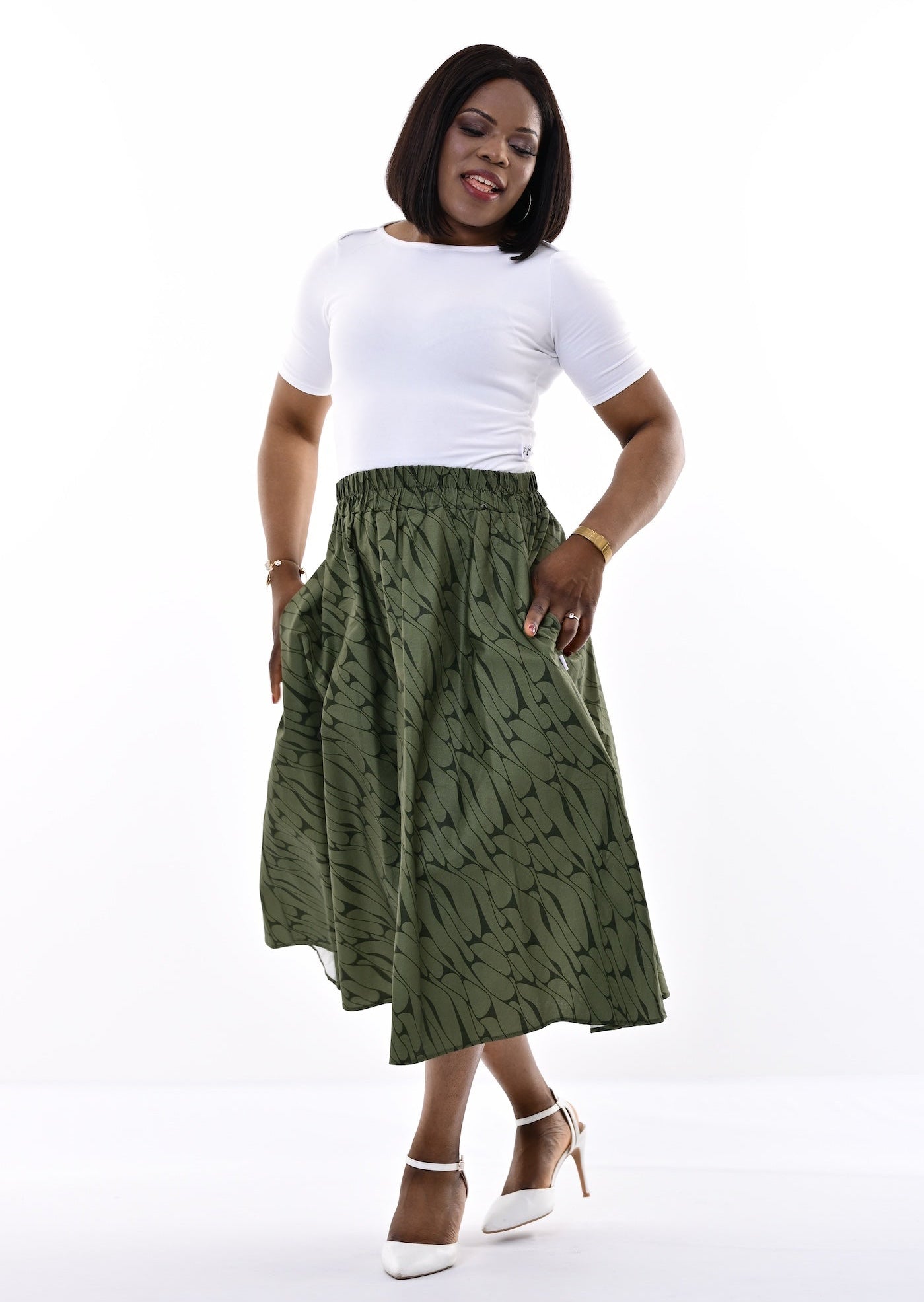 A woman modeling a white short-sleeve top and a green patterned midi skirt against a bright white studio background.