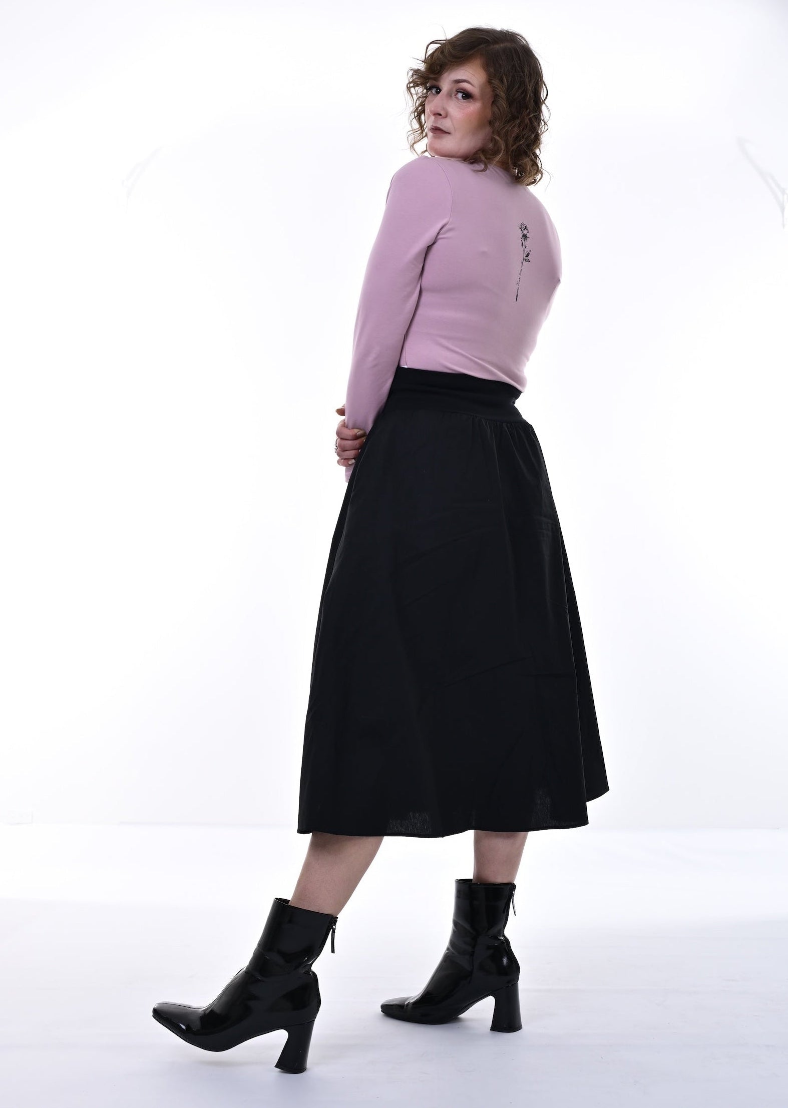 Woman wearing a pink sweater and black skirt on a white background
