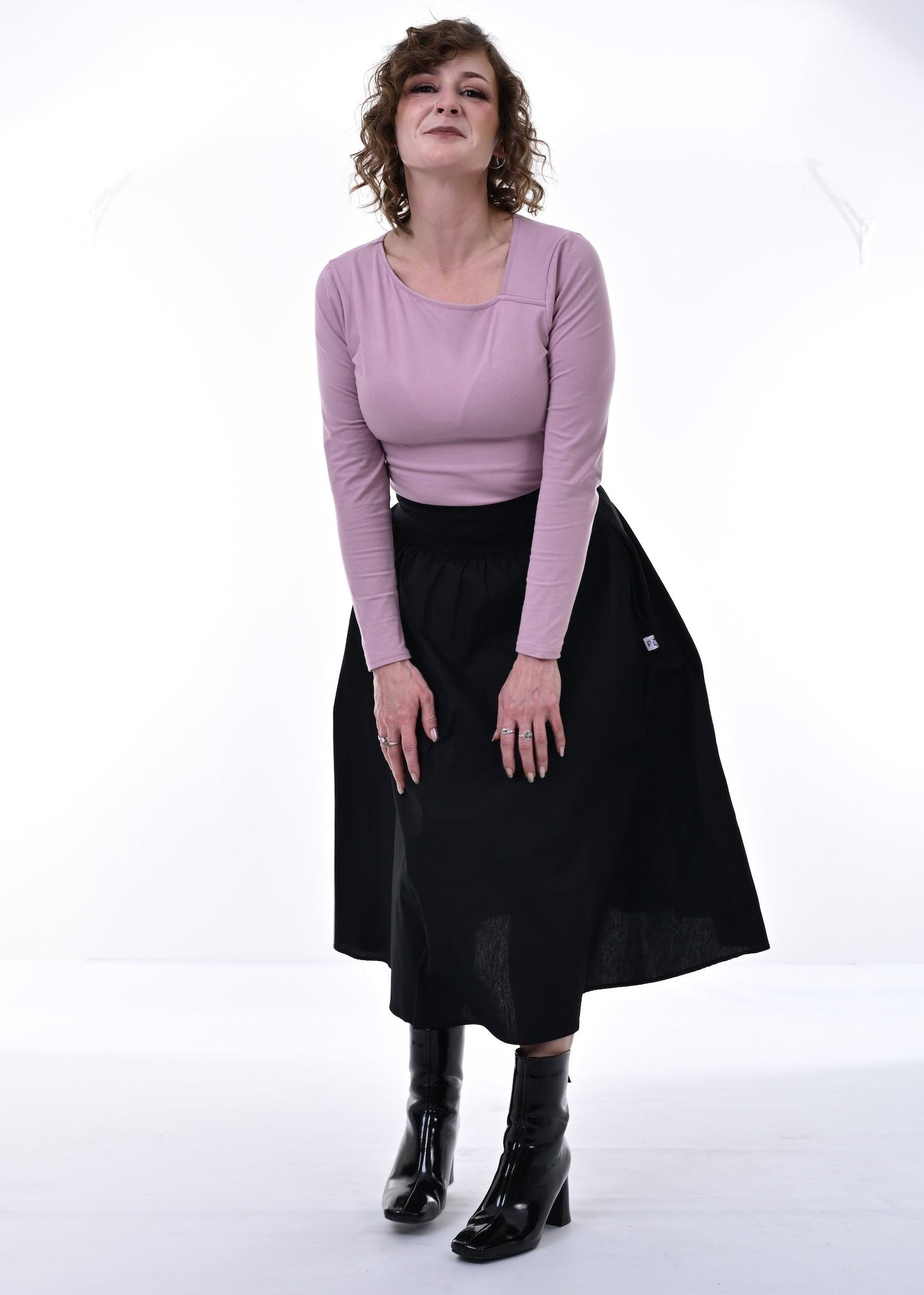 Woman wearing a pink top and black skirt standing against a white background