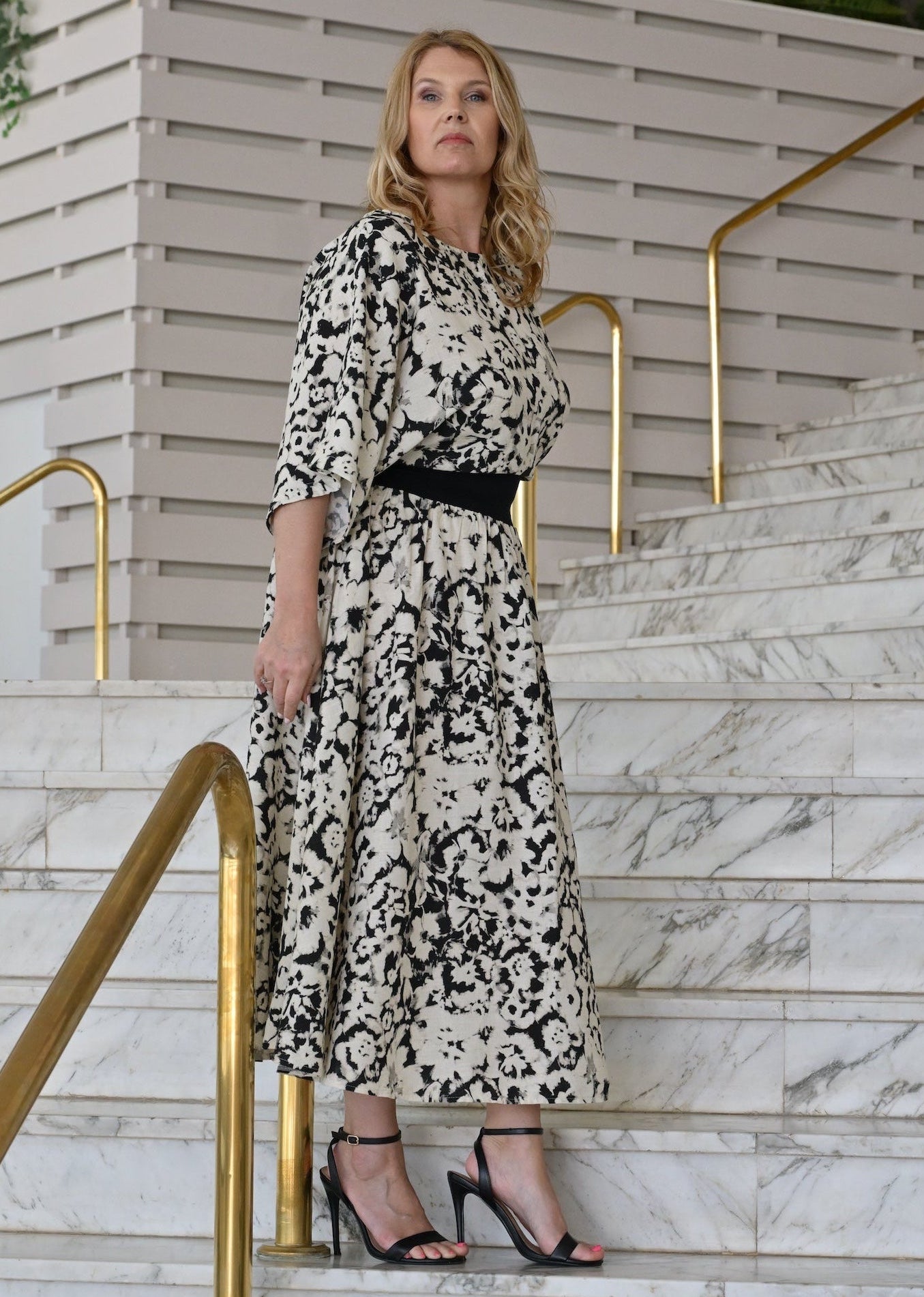 Woman in a black and white patterned dress standing on marble steps with gold railings.
