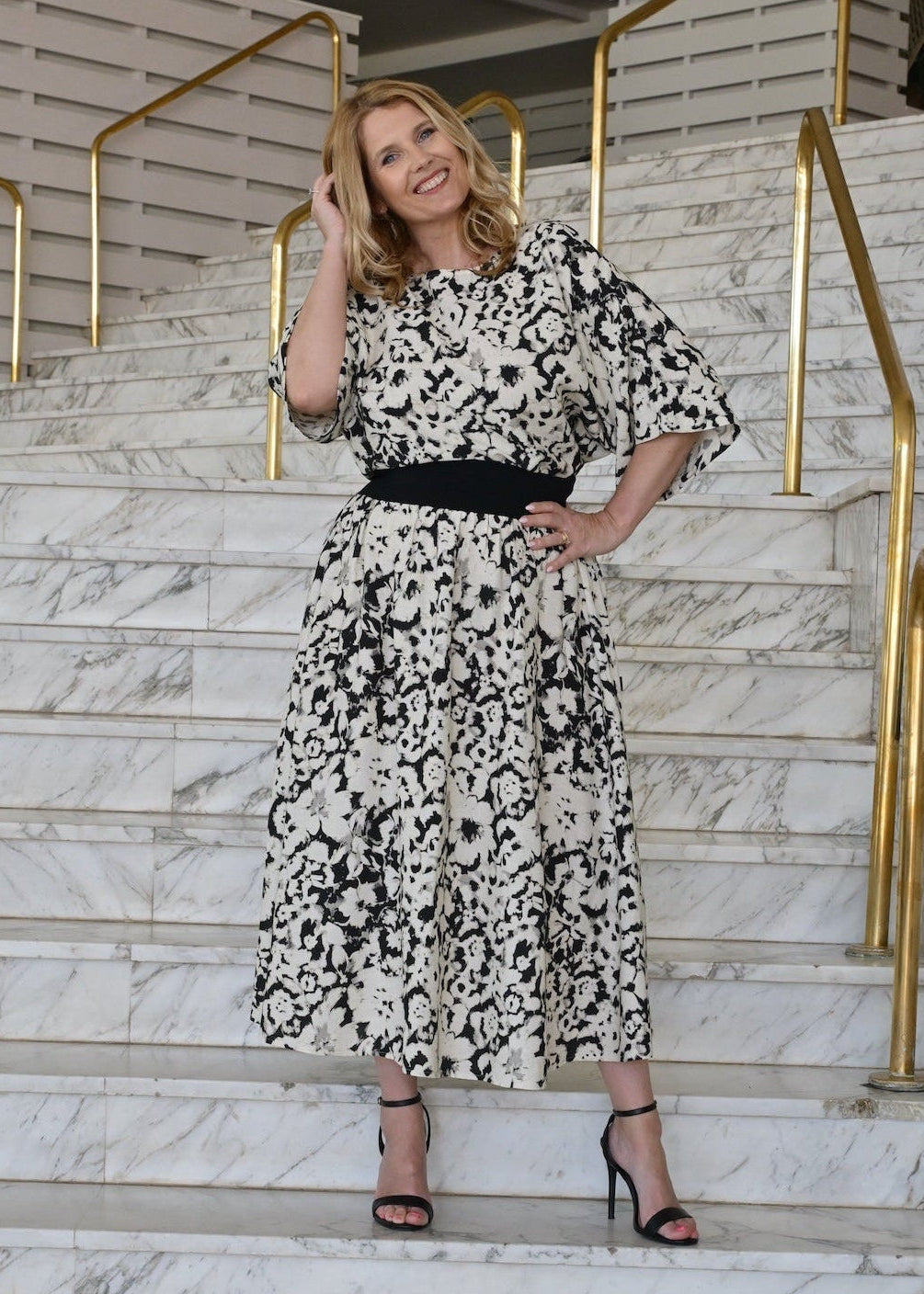 Woman in a floral dress standing on marble stairs with gold railings.