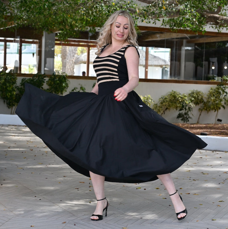Woman in a black and white striped top and black skirt twirling outdoors.