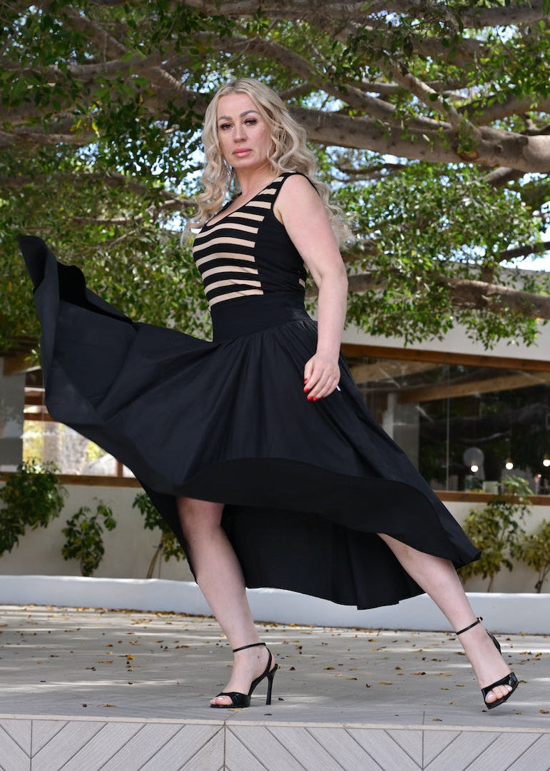 Woman in a black and white striped dress with a long black skirt standing on steps outdoors.