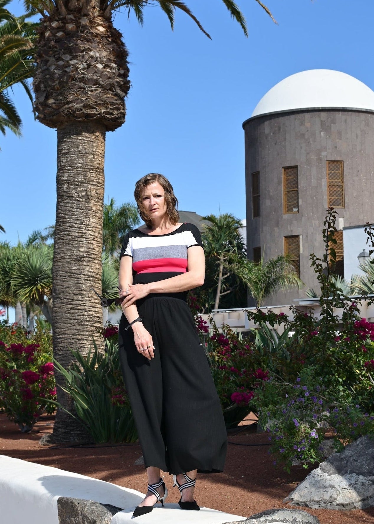 Woman standing in a garden with palm trees and a building in the background