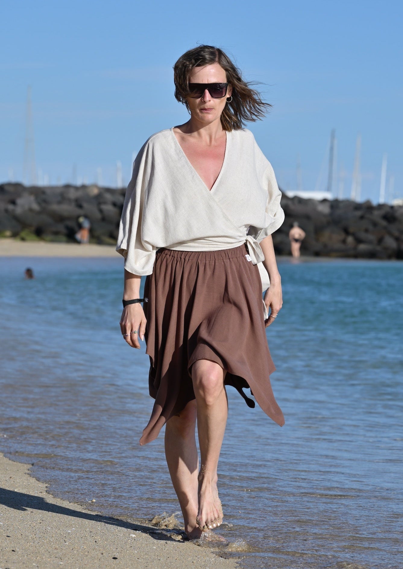 Woman walking on a beach with a clear blue sky and water in the background