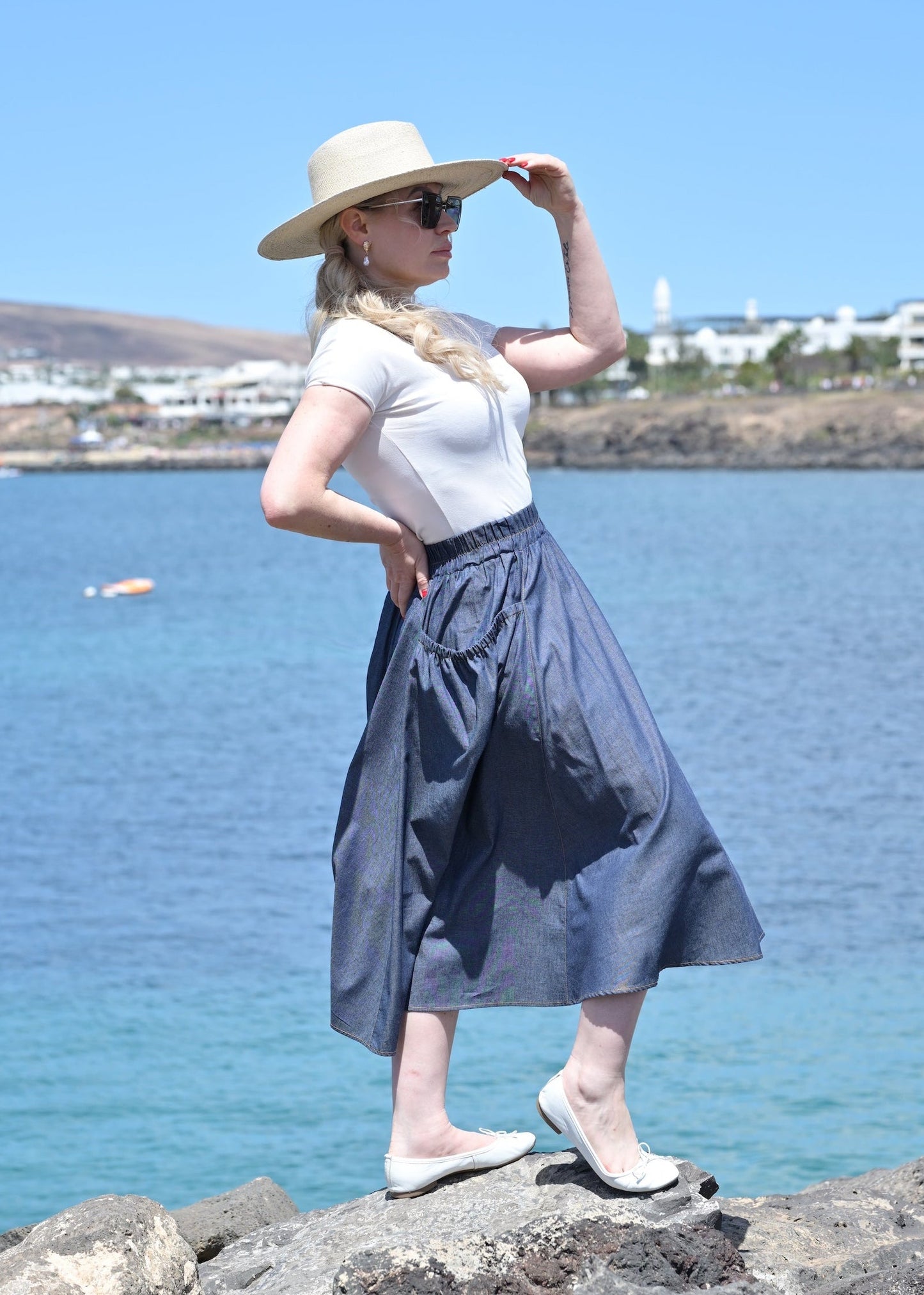 Woman in a white top and blue skirt standing on rocks by the sea
