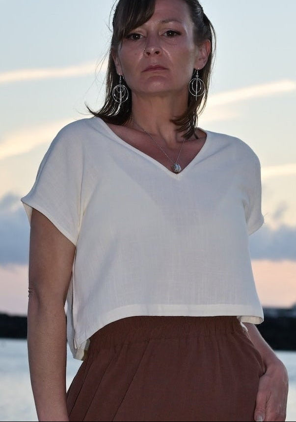 Woman standing on a beach wearing a white top and brown skirt.