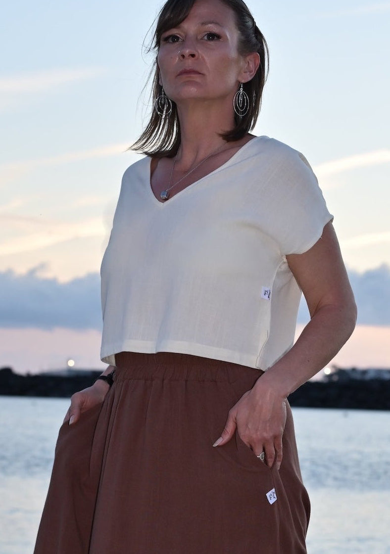 Woman in a white top and brown skirt standing on a beach at sunset.