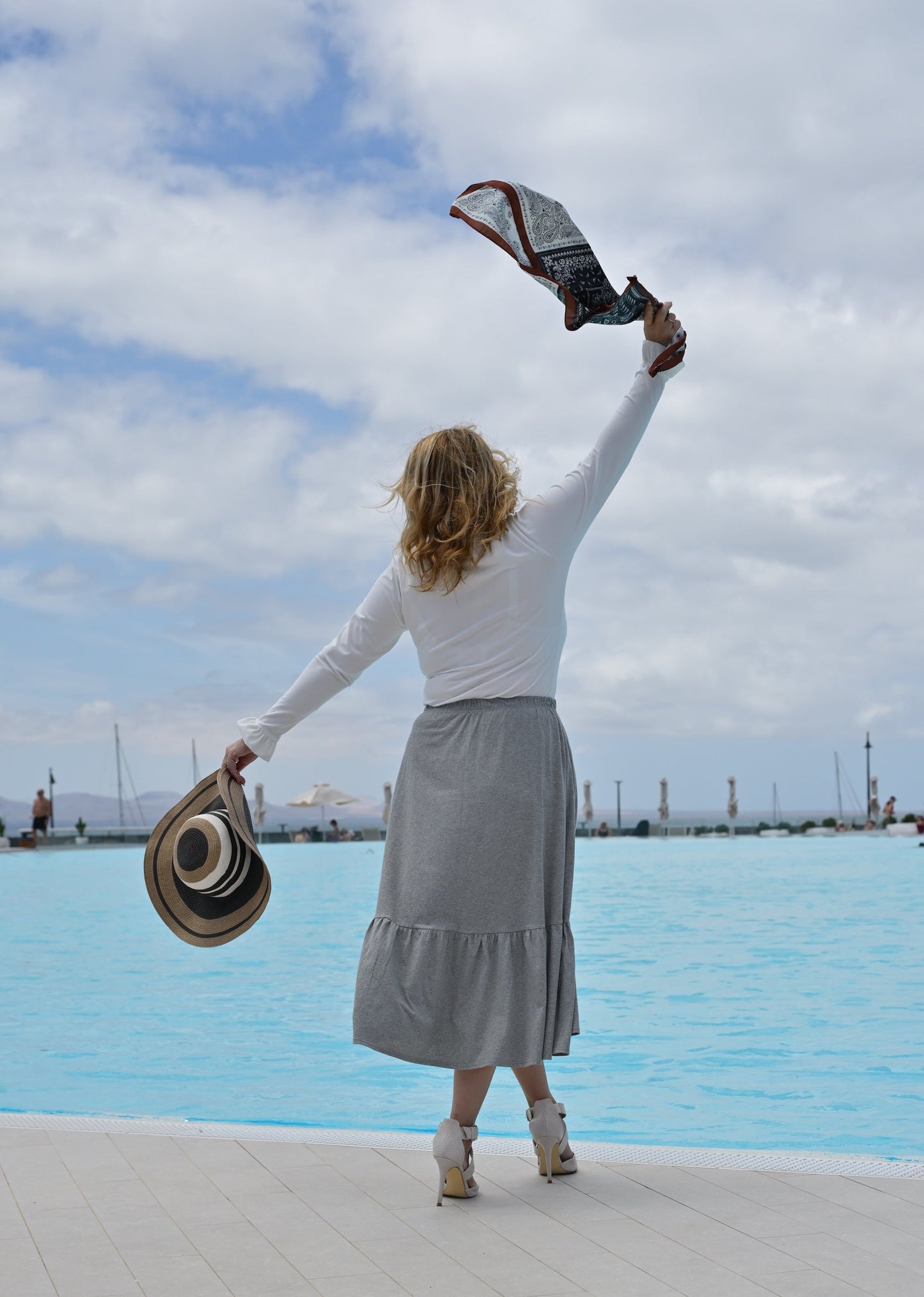 Woman standing by a pool with a blue sky and clouds in the background