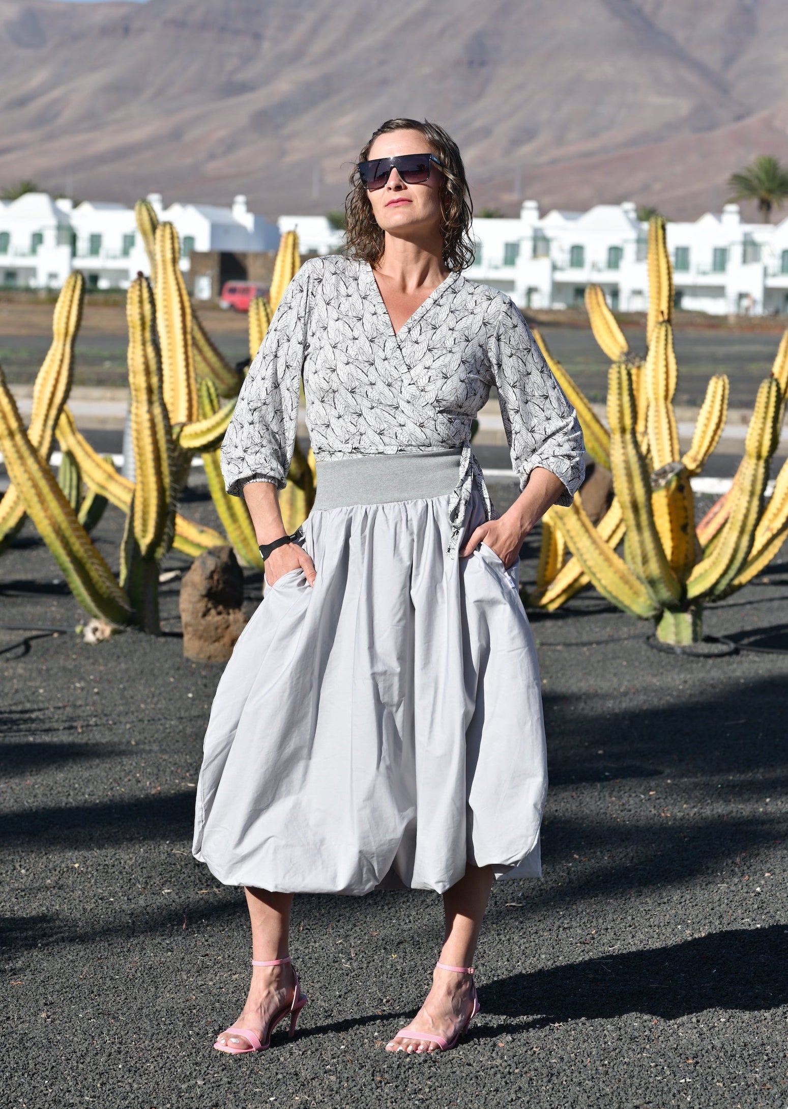 Woman in a light dress standing in front of large cacti and mountains.