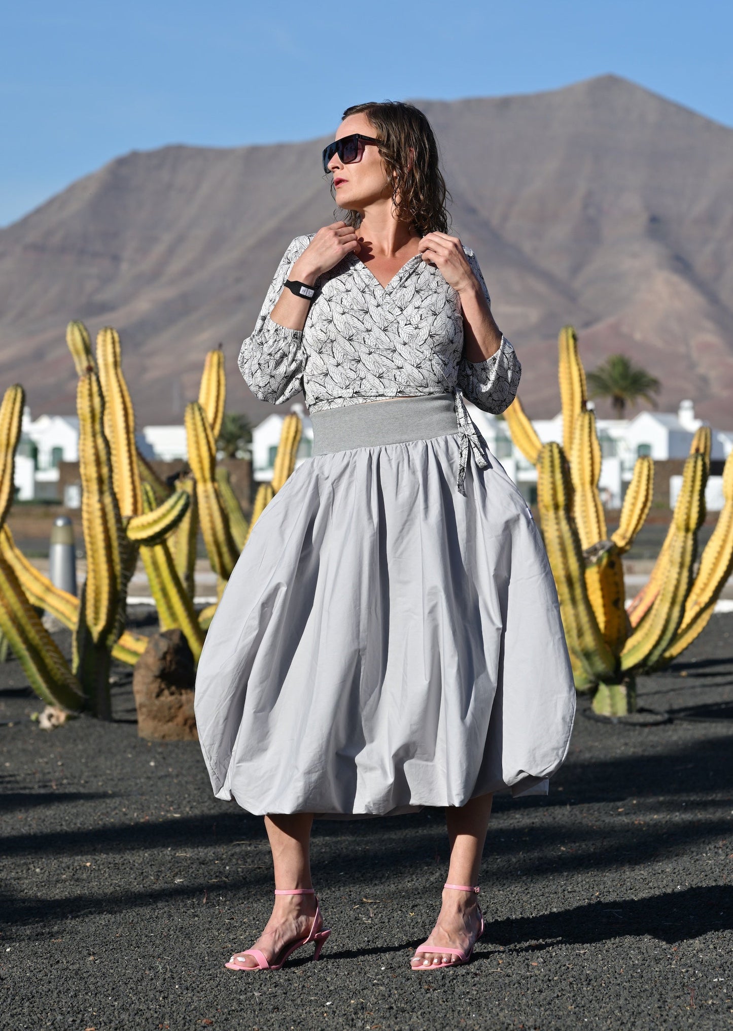 Woman in a light gray dress standing in front of cacti and mountains.