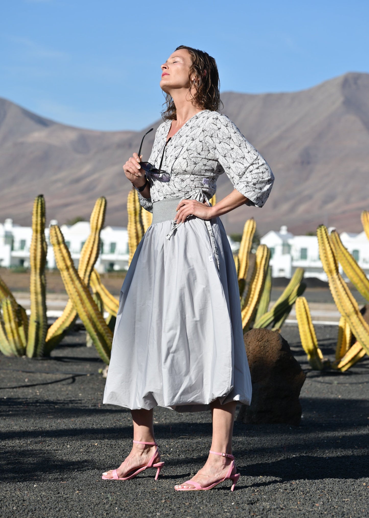 Woman in a patterned dress standing in front of cacti with mountains in the background