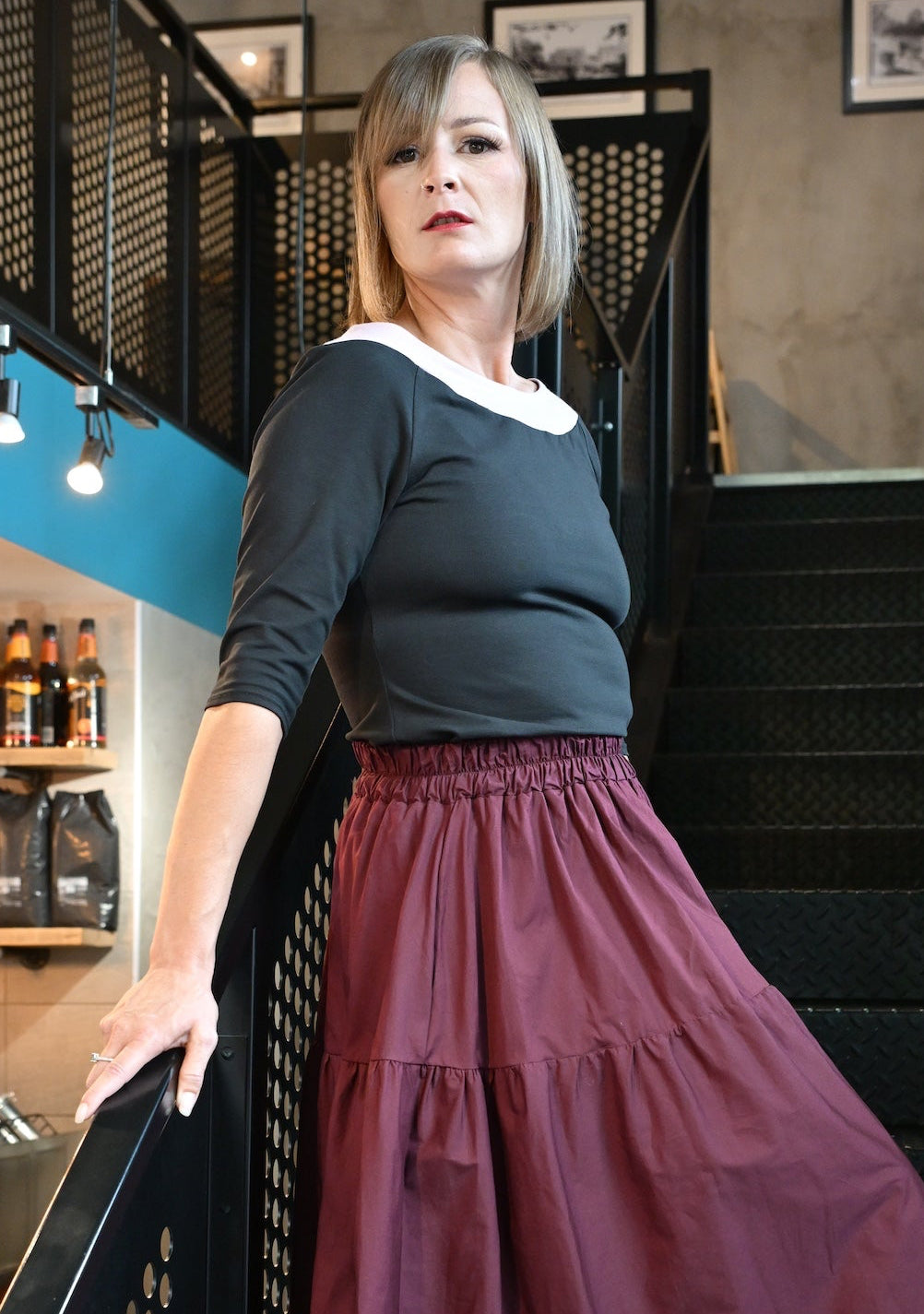 Woman in a dark top and red skirt standing in a modern interior setting.