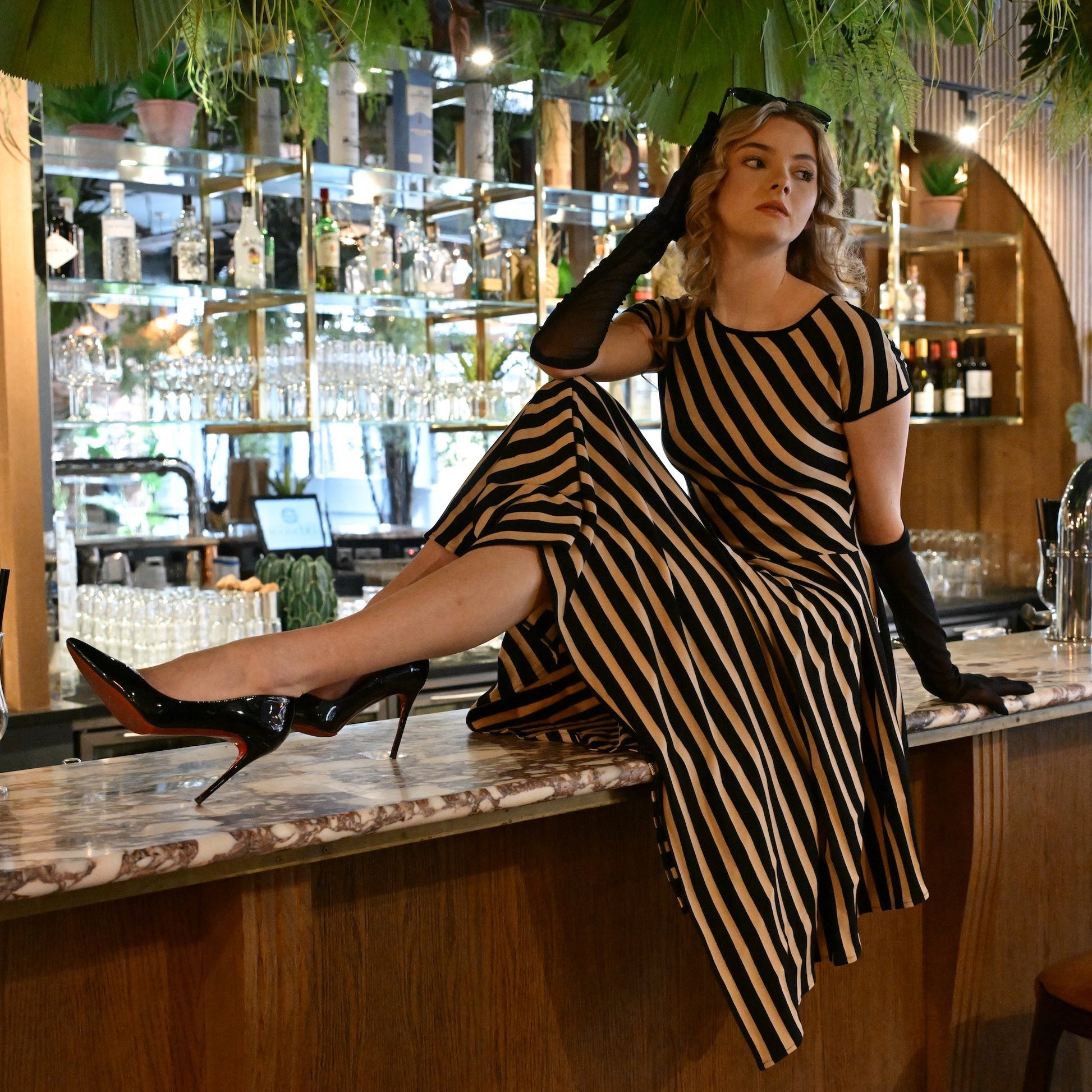 Woman in a striped dress leaning on a bar counter in a stylish bar setting.