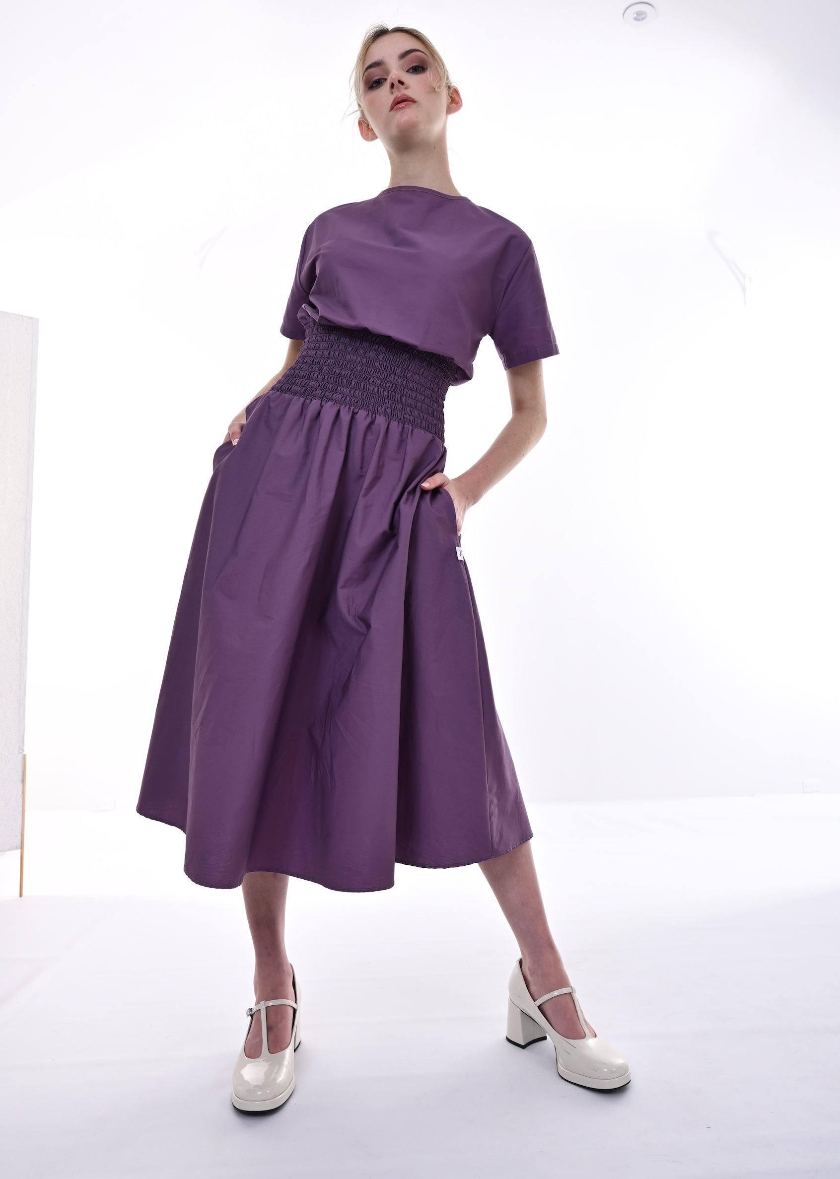 Woman wearing a purple outfit with a top and skirt in a studio setting