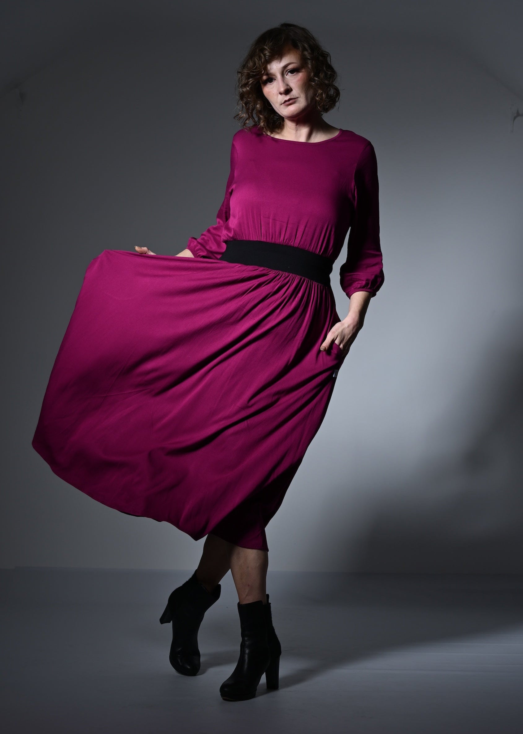 Woman wearing a magenta dress with a black belt against a gray background