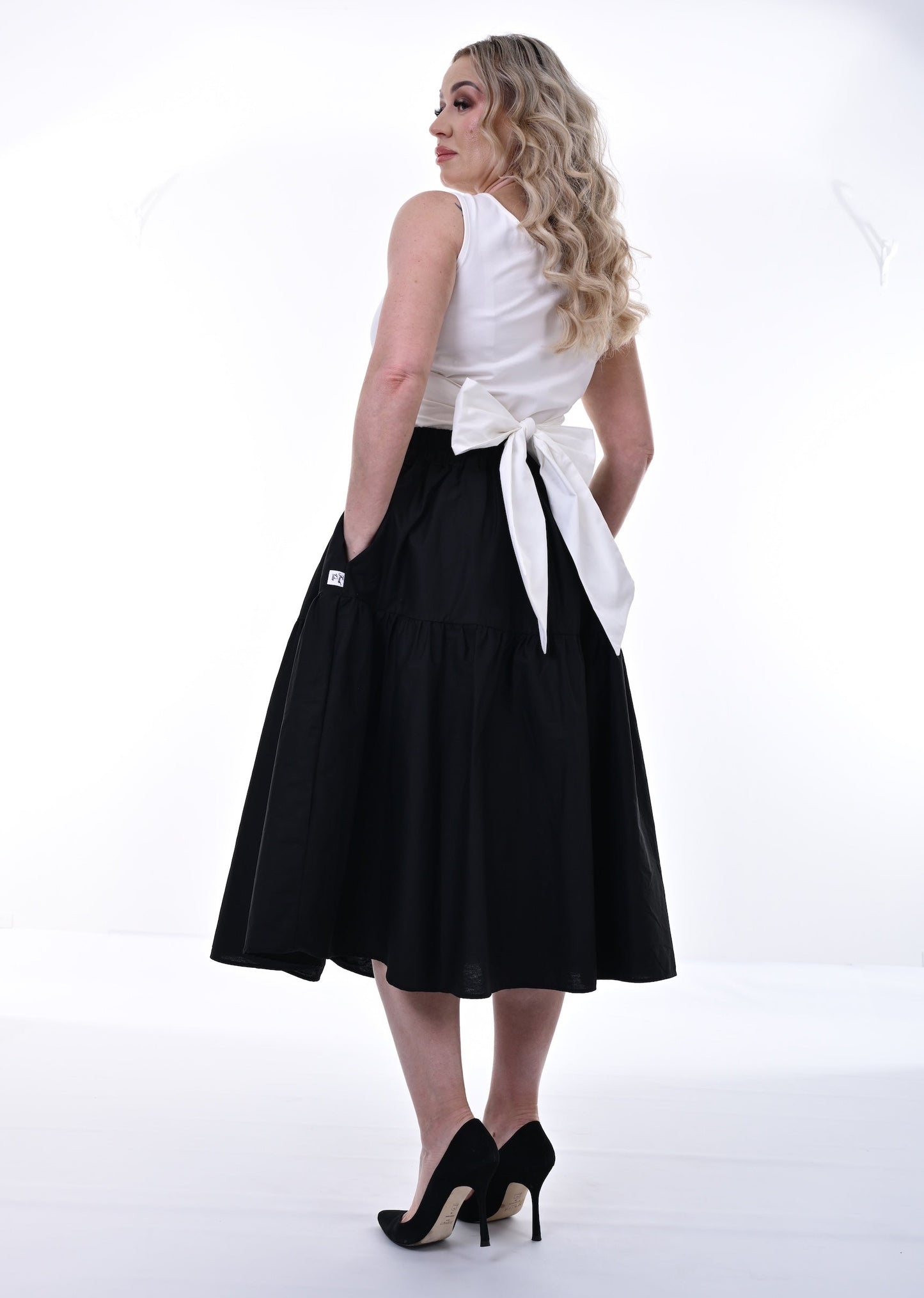 Woman wearing a white sleeveless top and black skirt with a white belt on a white background