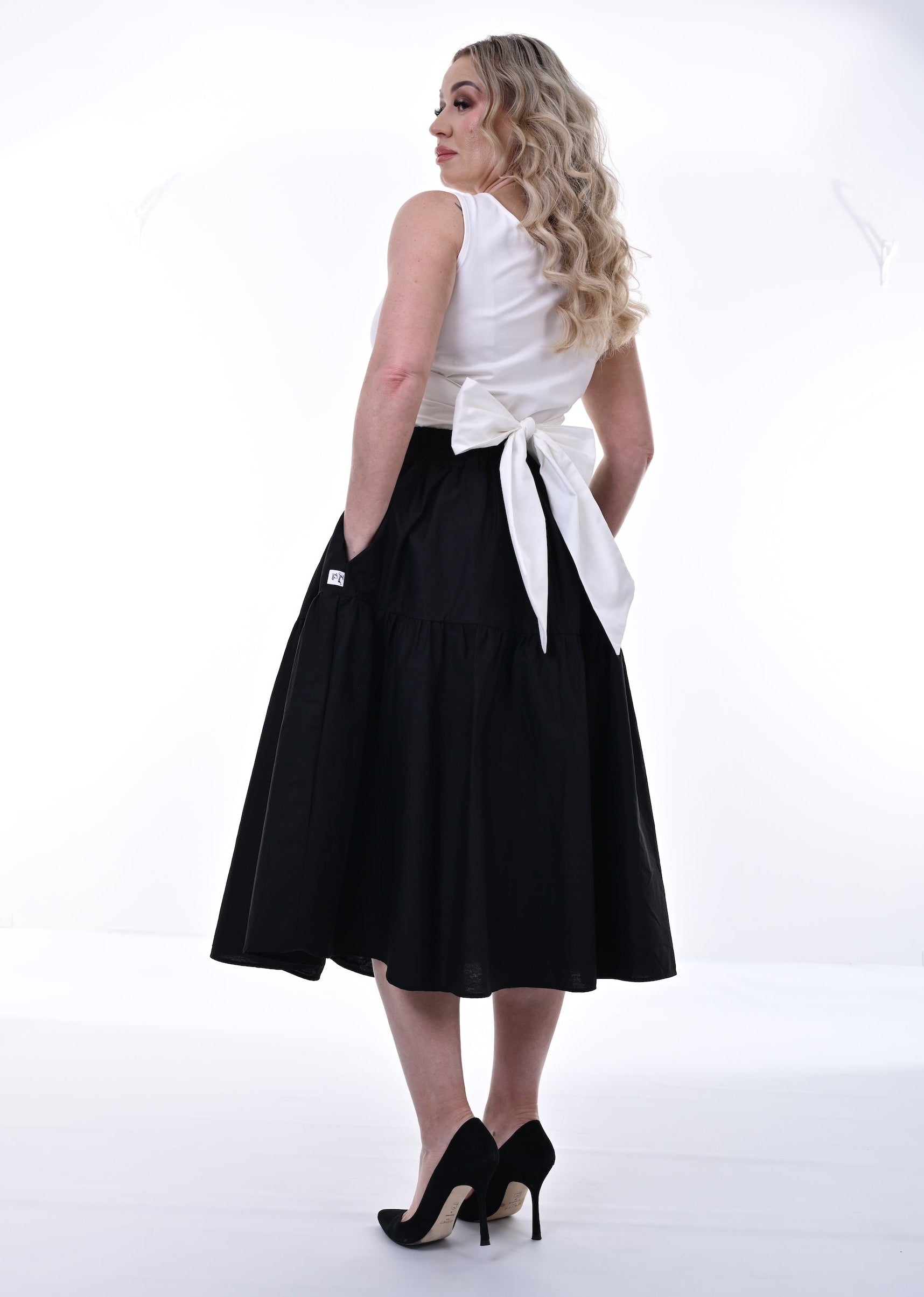 Woman wearing a white sleeveless top and black skirt with a white belt on a white background