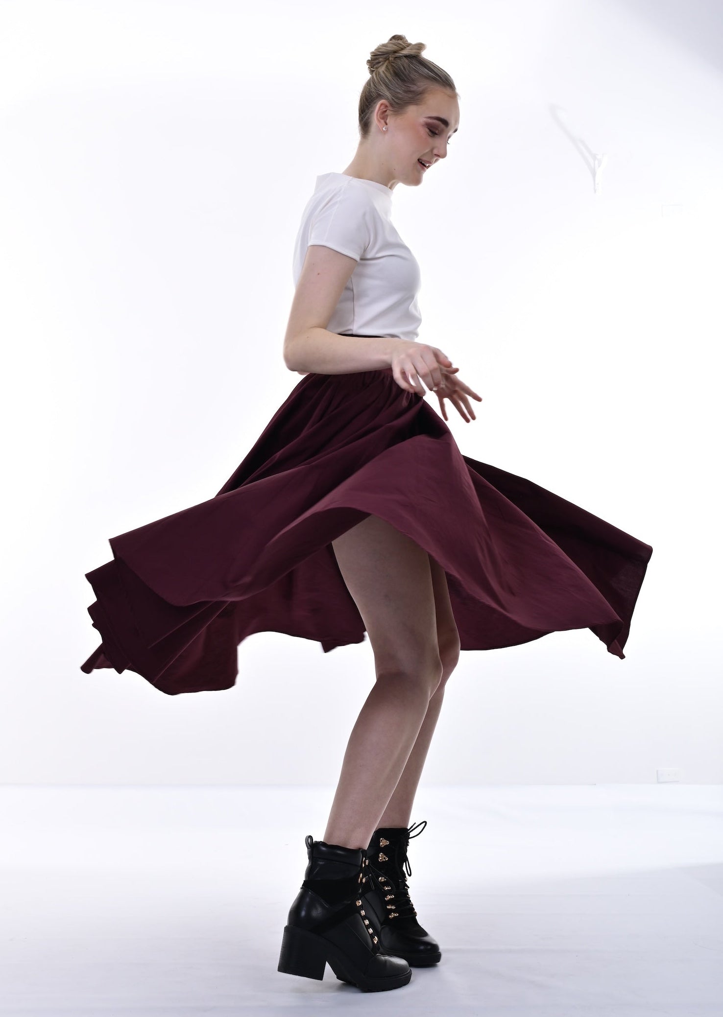 Woman in a white top and burgundy skirt with black boots on a white background