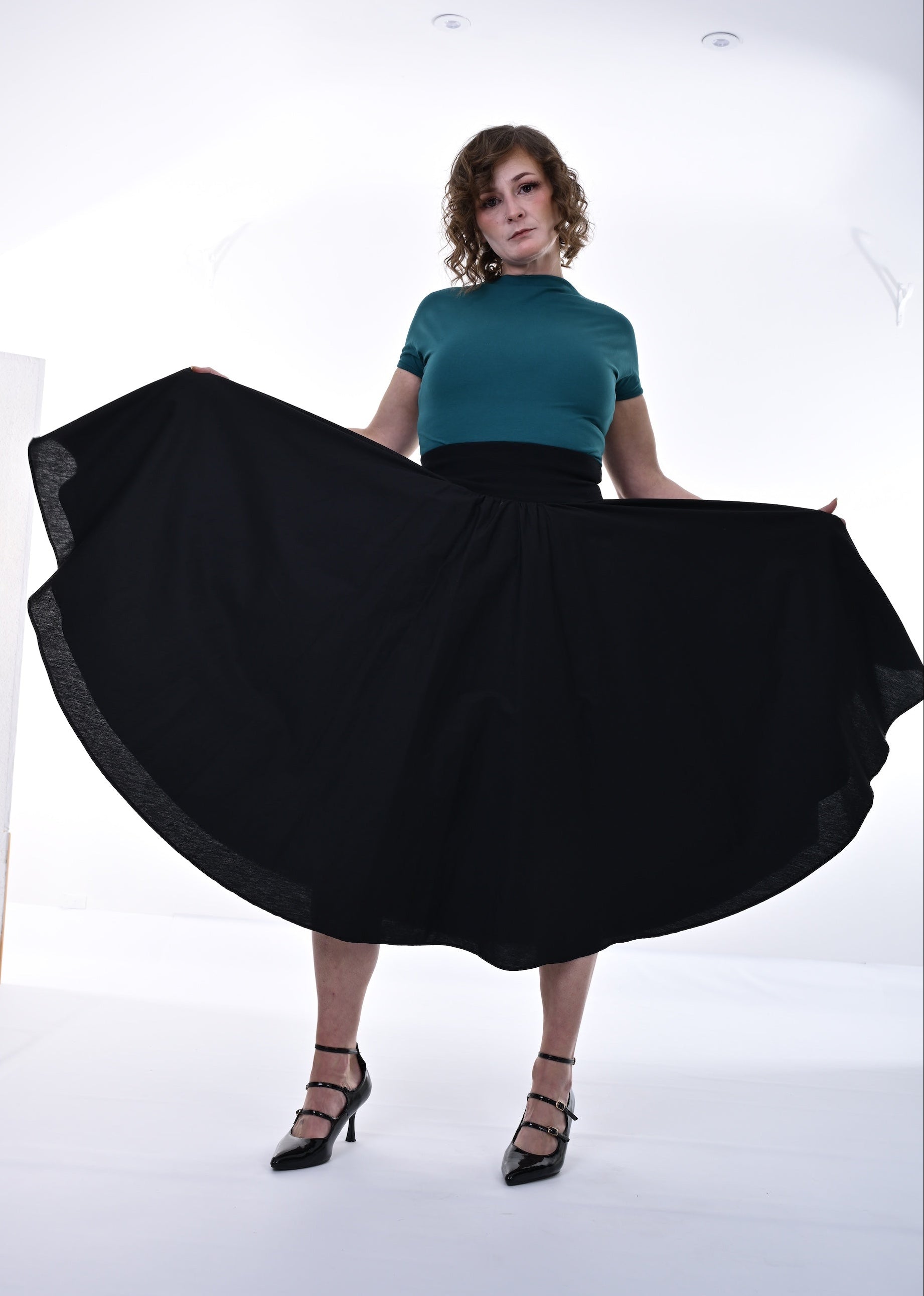 Woman wearing a teal top and black skirt in a studio setting